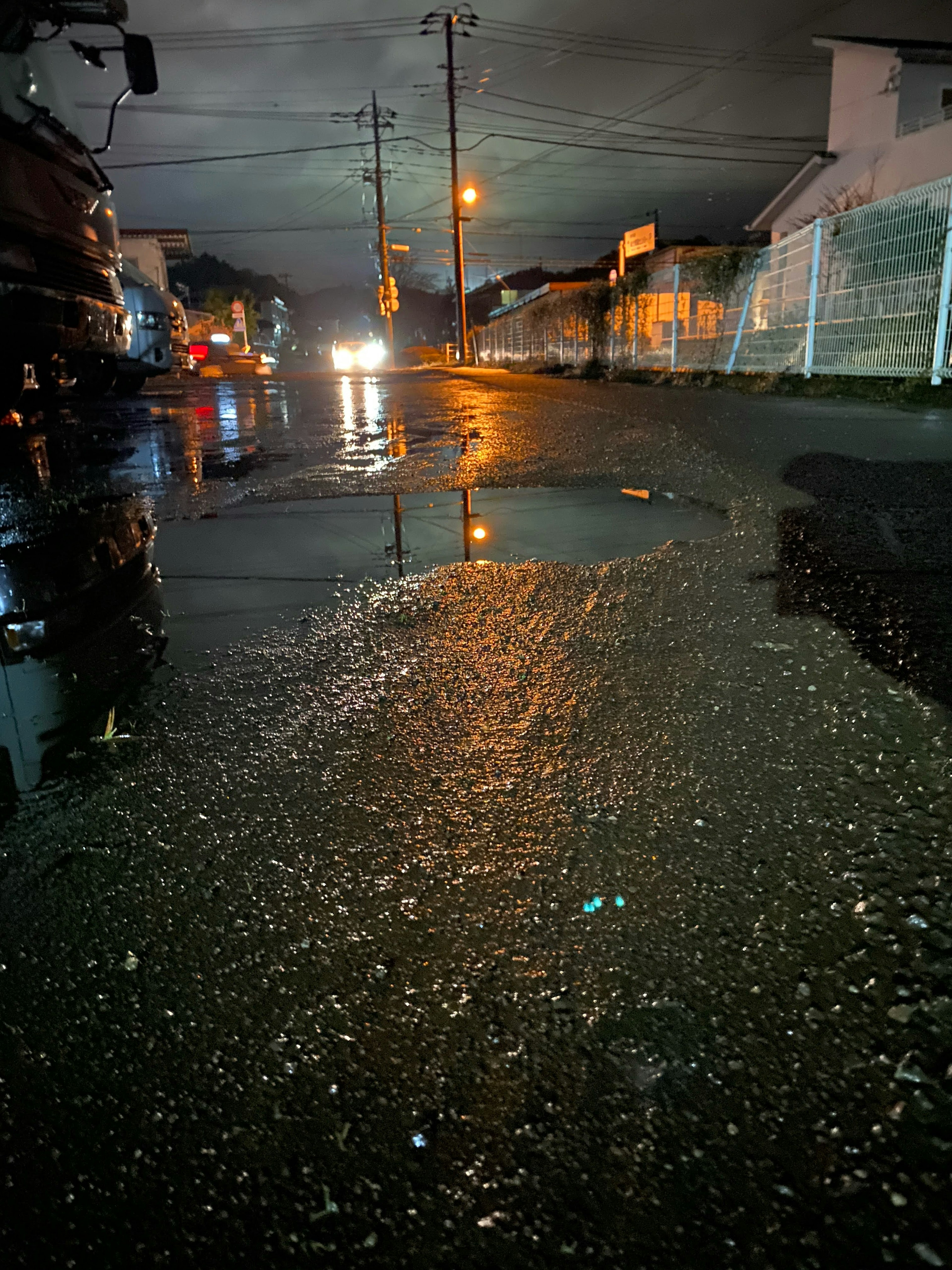 Strada di notte con pozzanghere che riflettono luci e nuvole scure