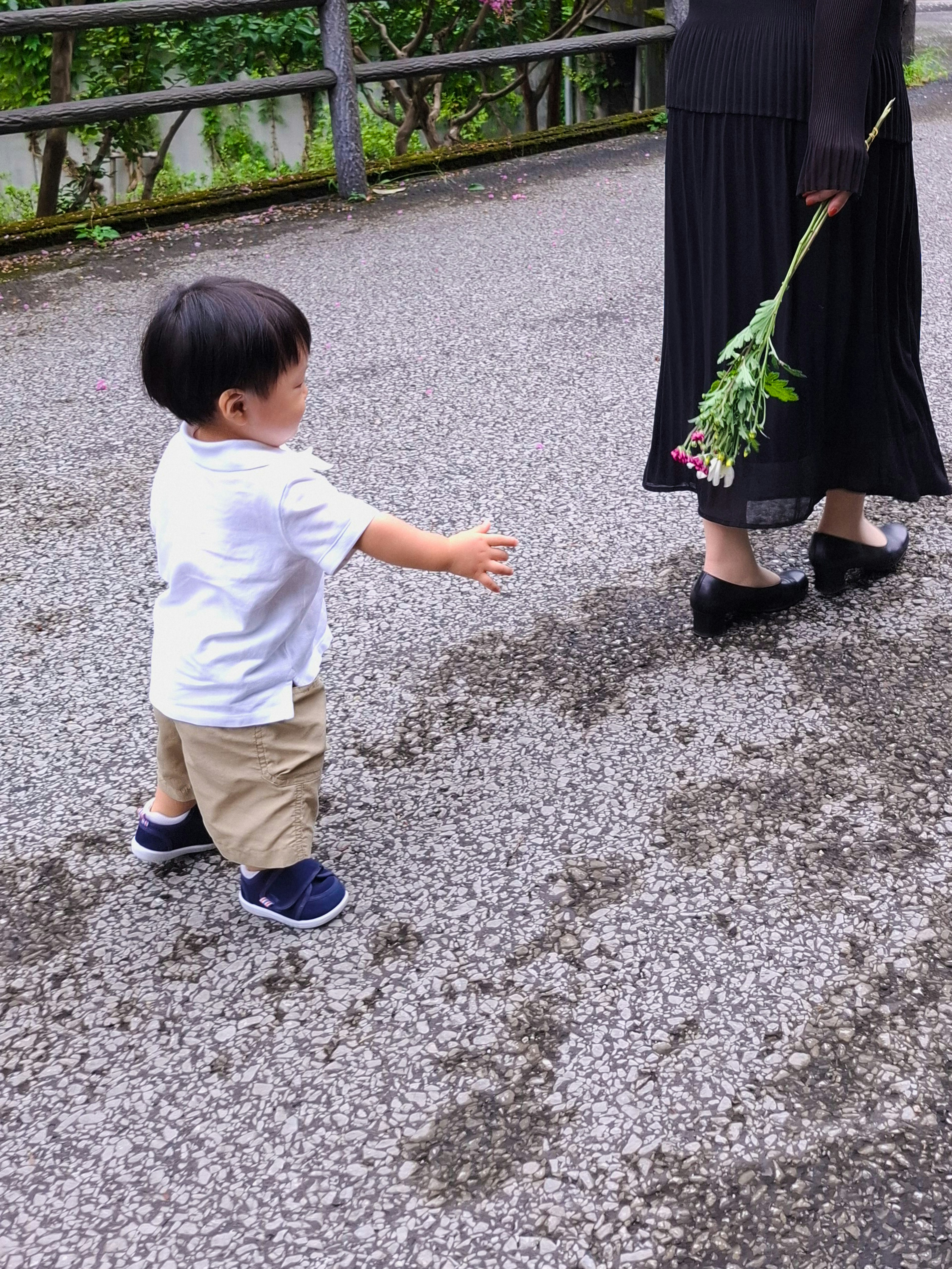 Ein Kind in einem weißen Shirt, das auf eine Frau zugeht, die Blumen hält