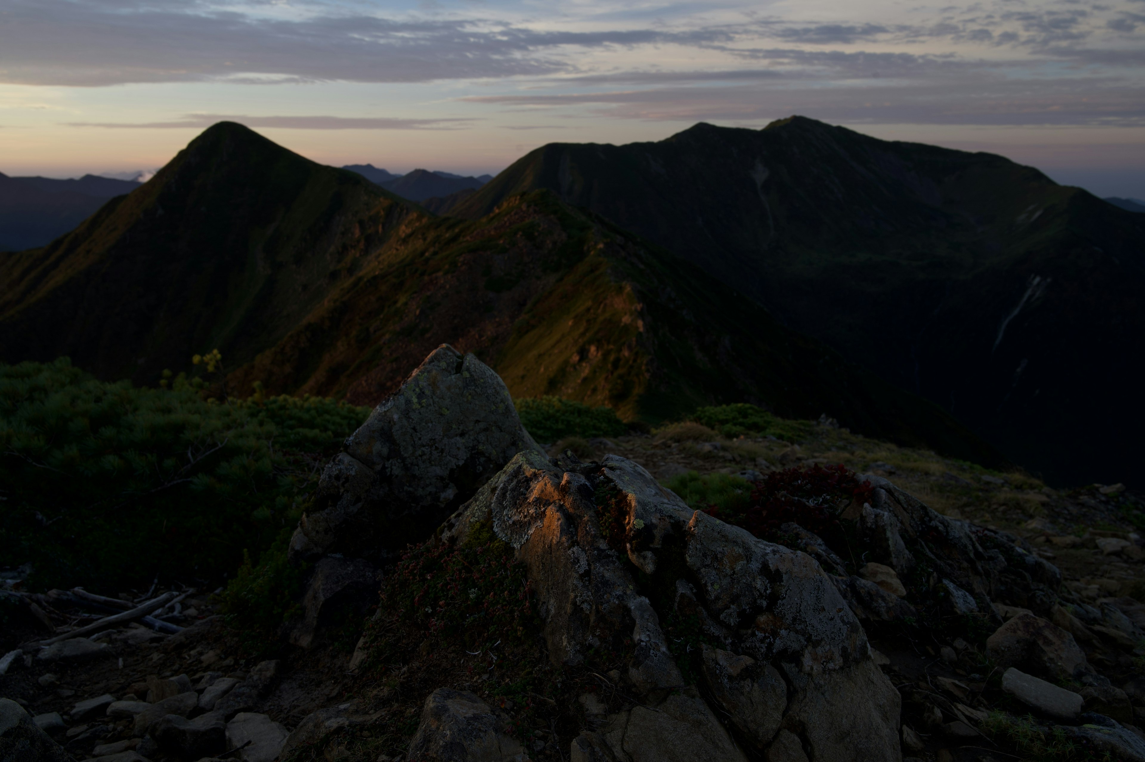 夕暮れ時の山の風景で、岩と緑の草が見える