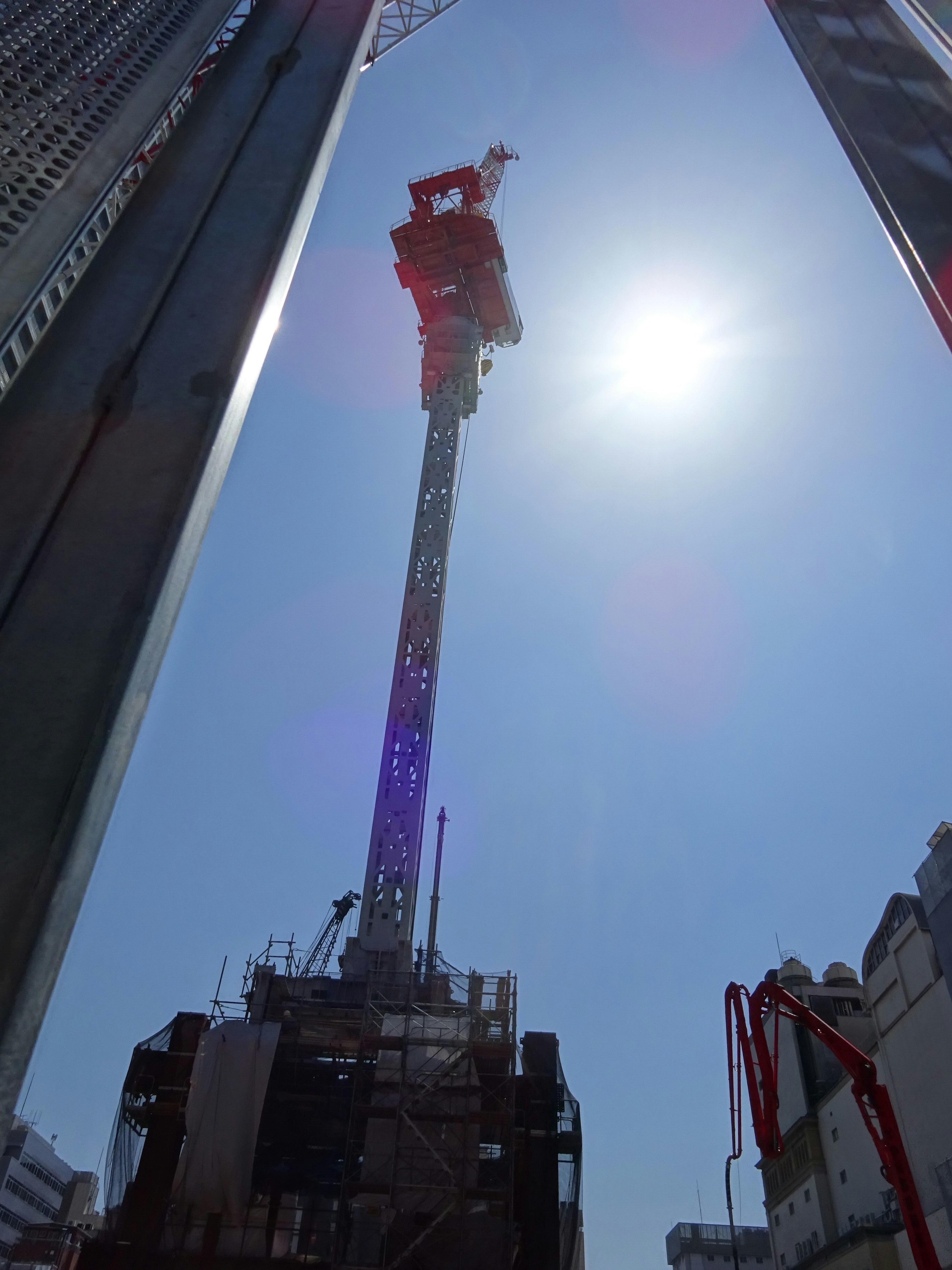 Construction crane towering between high-rise buildings under a bright sun