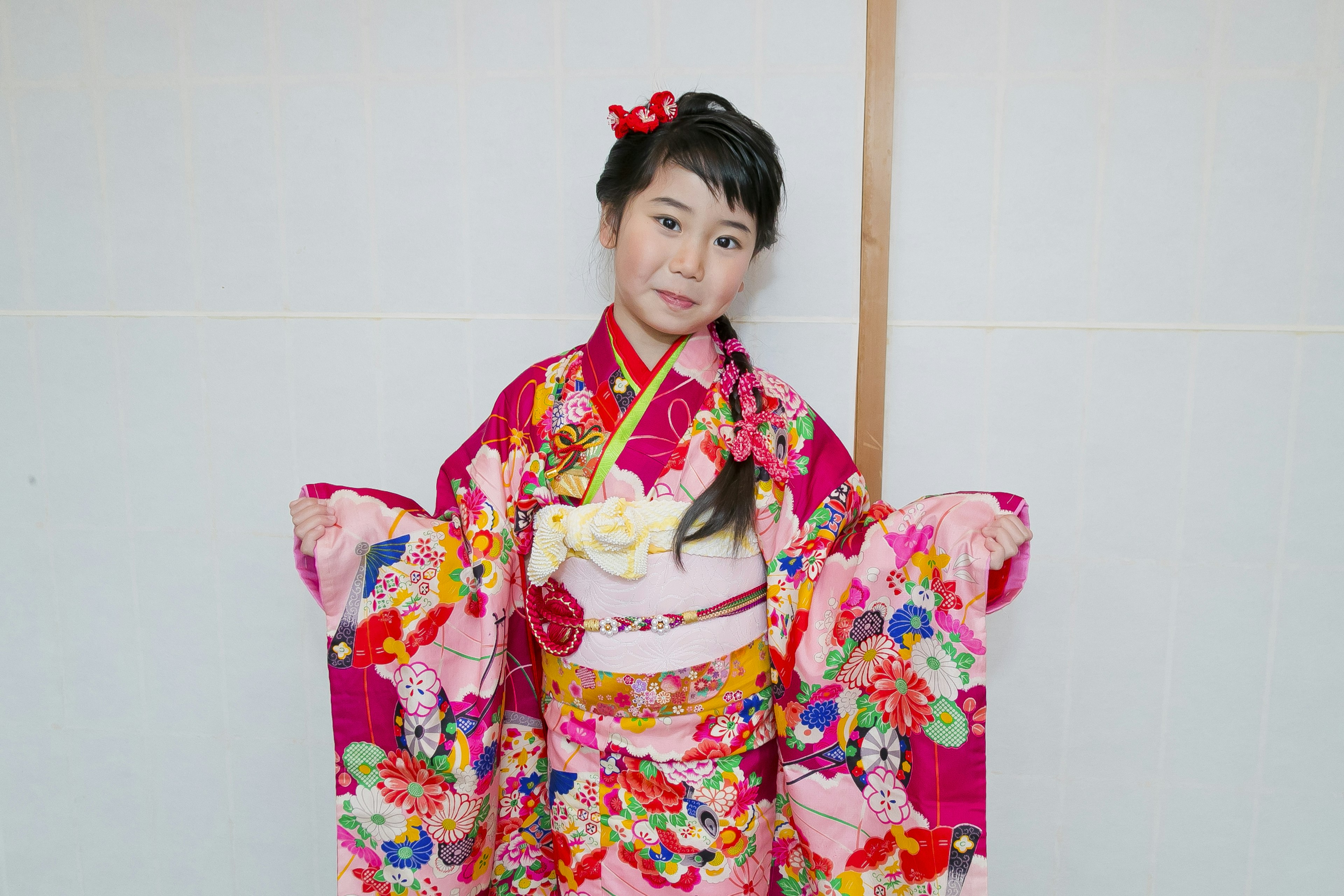 Gadis dalam kimono pink cerah tersenyum dalam pose tradisional