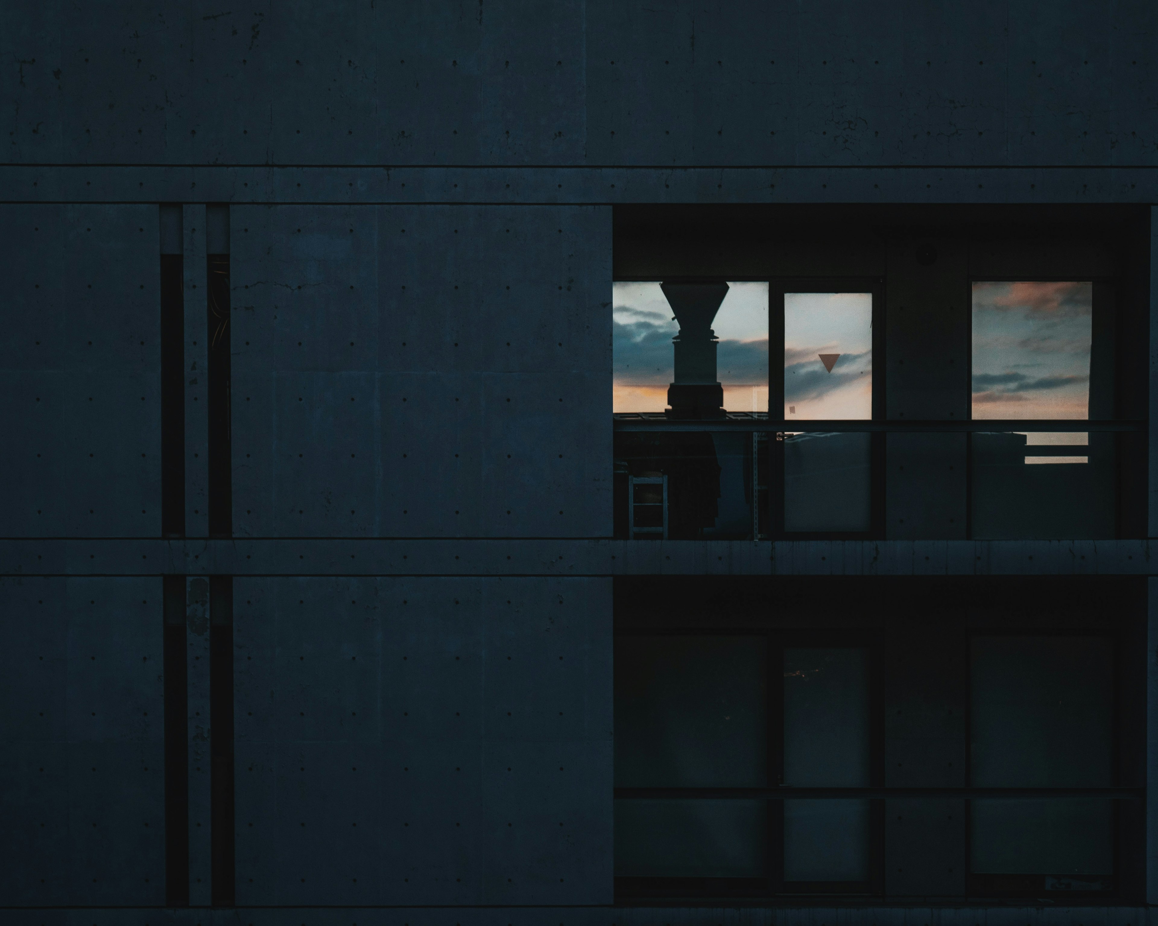 Dark building with windows showing a sunset sky and a chair