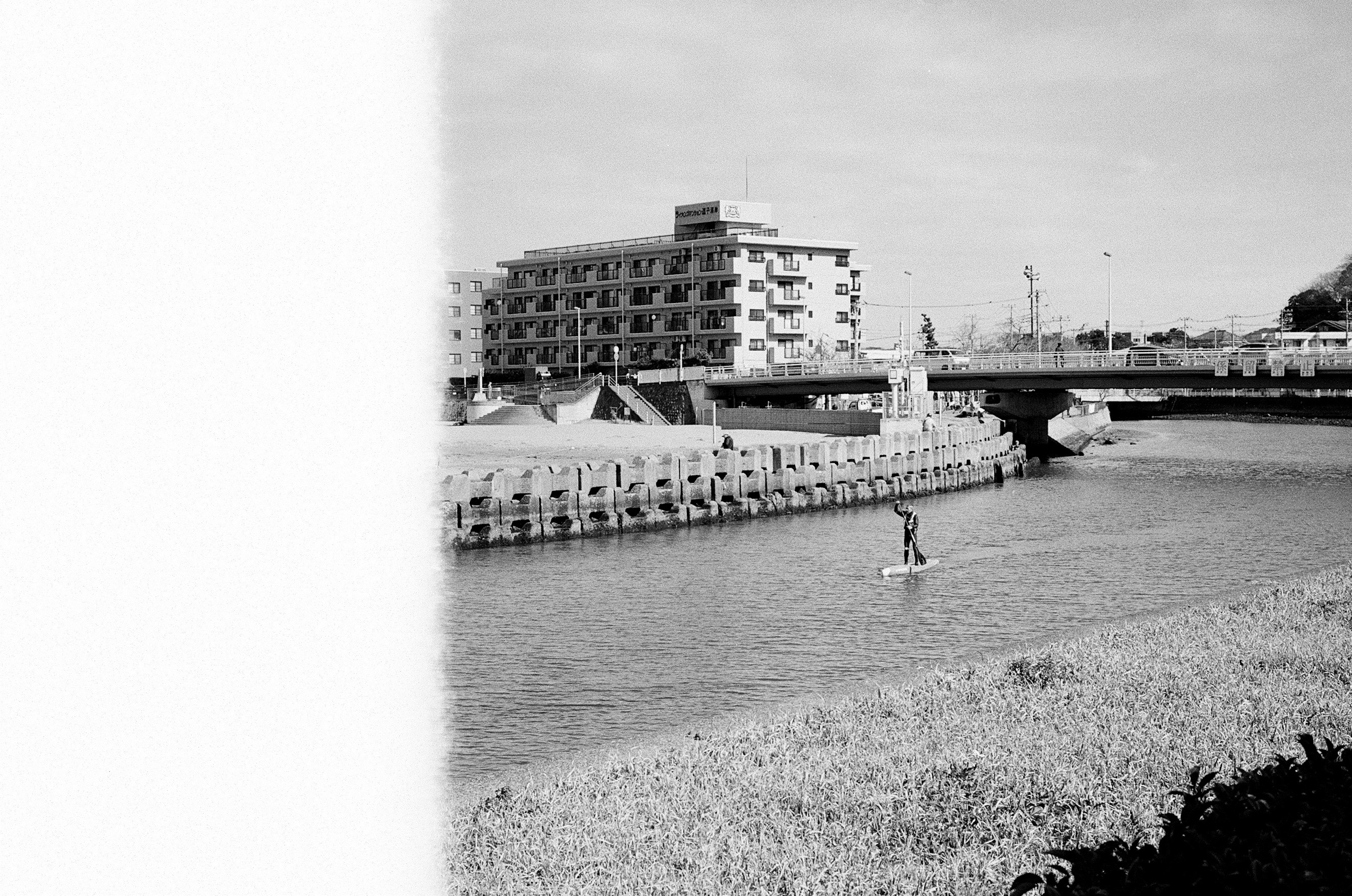 白黒の川に沿って立ち漕ぎをしている人が見える都市の風景