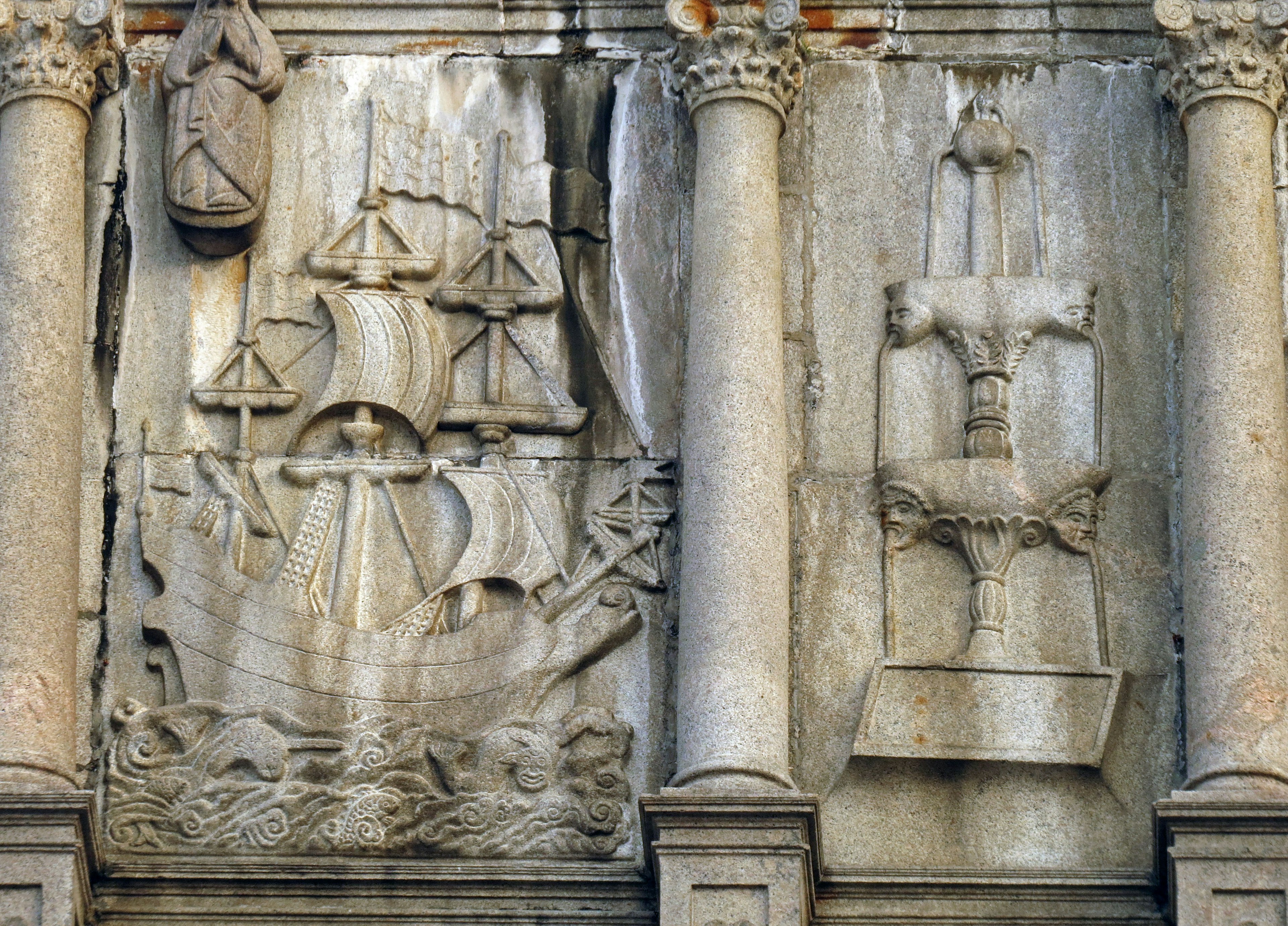 Steinwand mit Reliefs von Schiffen und einem Kreuz