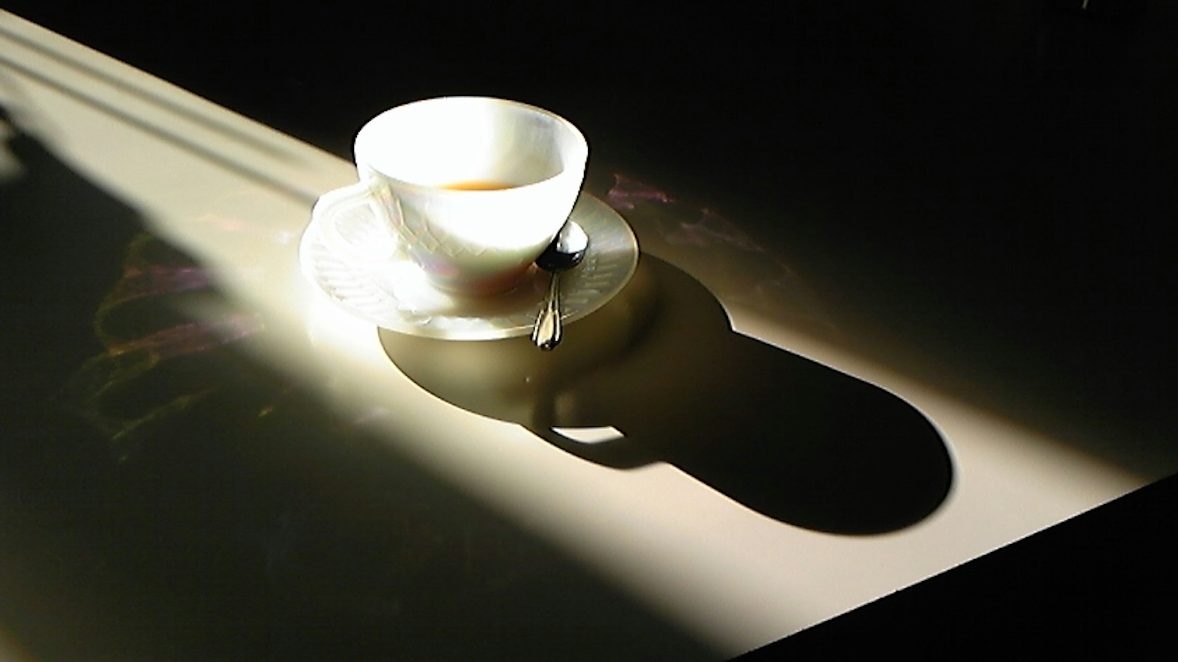 Una taza blanca y un platillo colocados en la luz proyectando una sombra