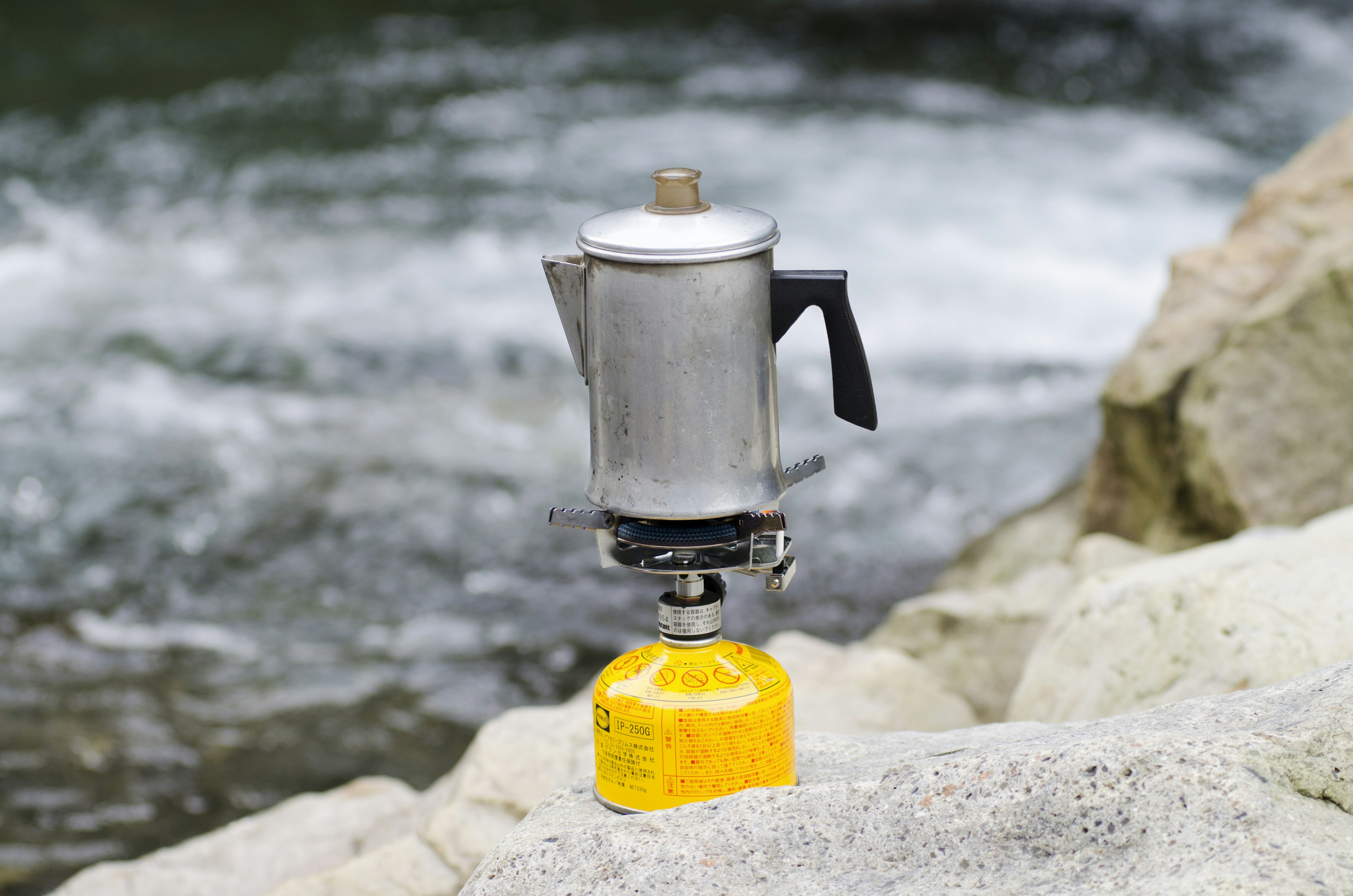 Silberne Kaffeekanne auf gelbem Gaskanister am Fluss