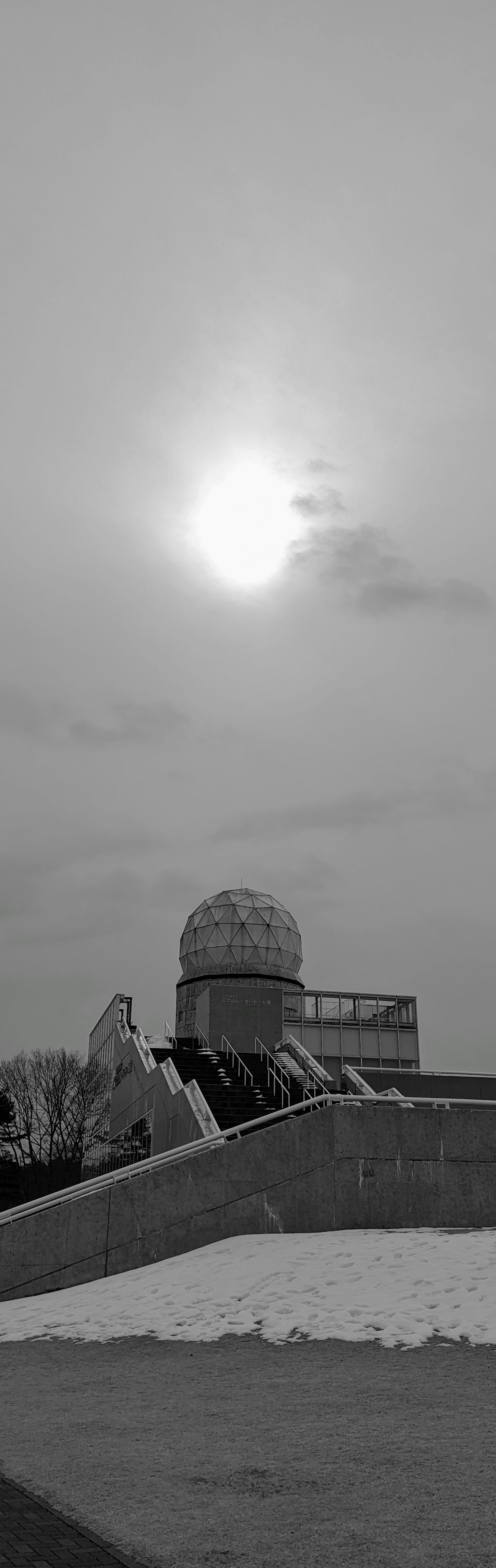 Silhouette eines kuppelartigen Gebäudes vor einem monochromen Himmel mit der Sonne