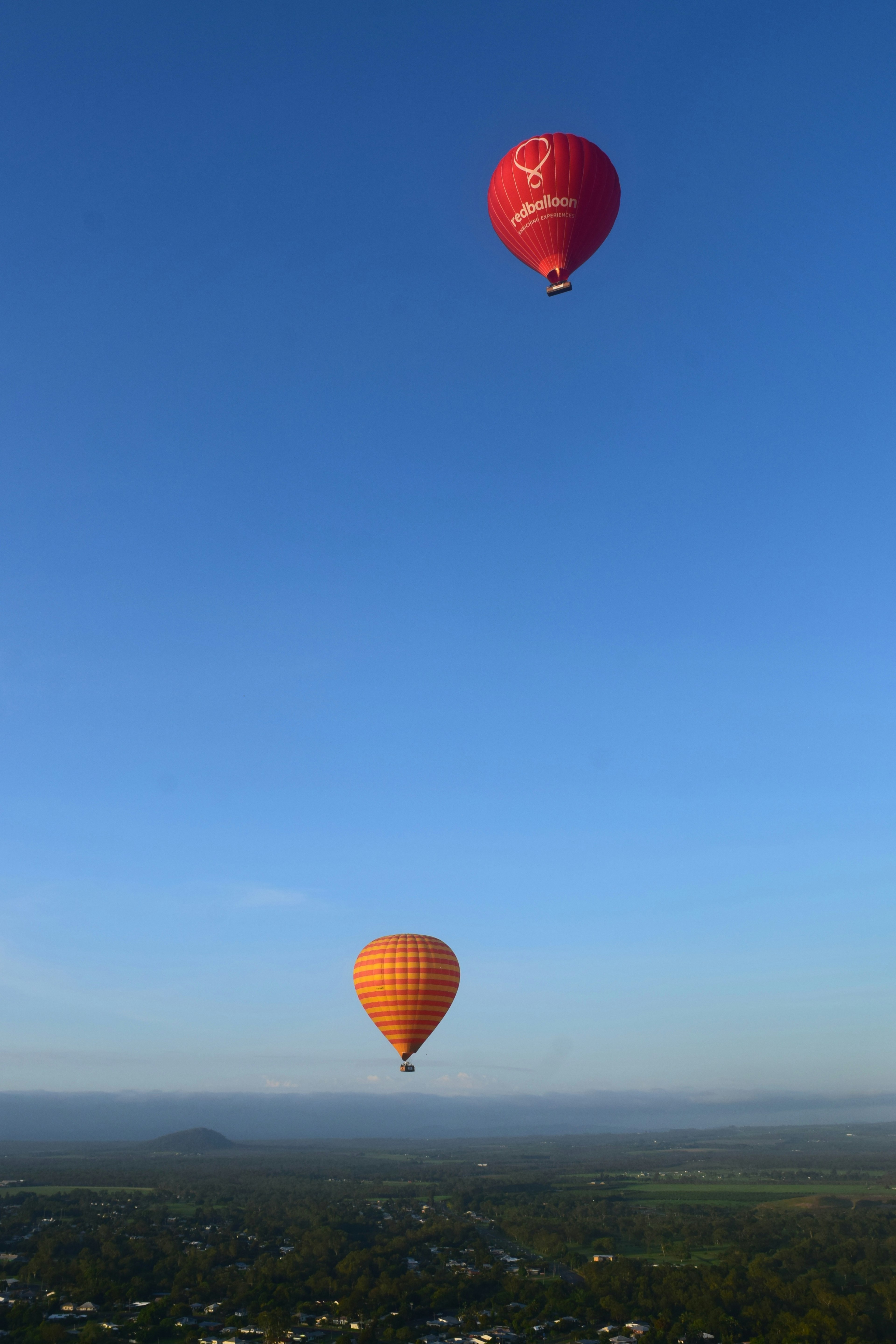 Szene mit einem roten Heißluftballon und einem orangefarbenen Heißluftballon, die in einem blauen Himmel schweben