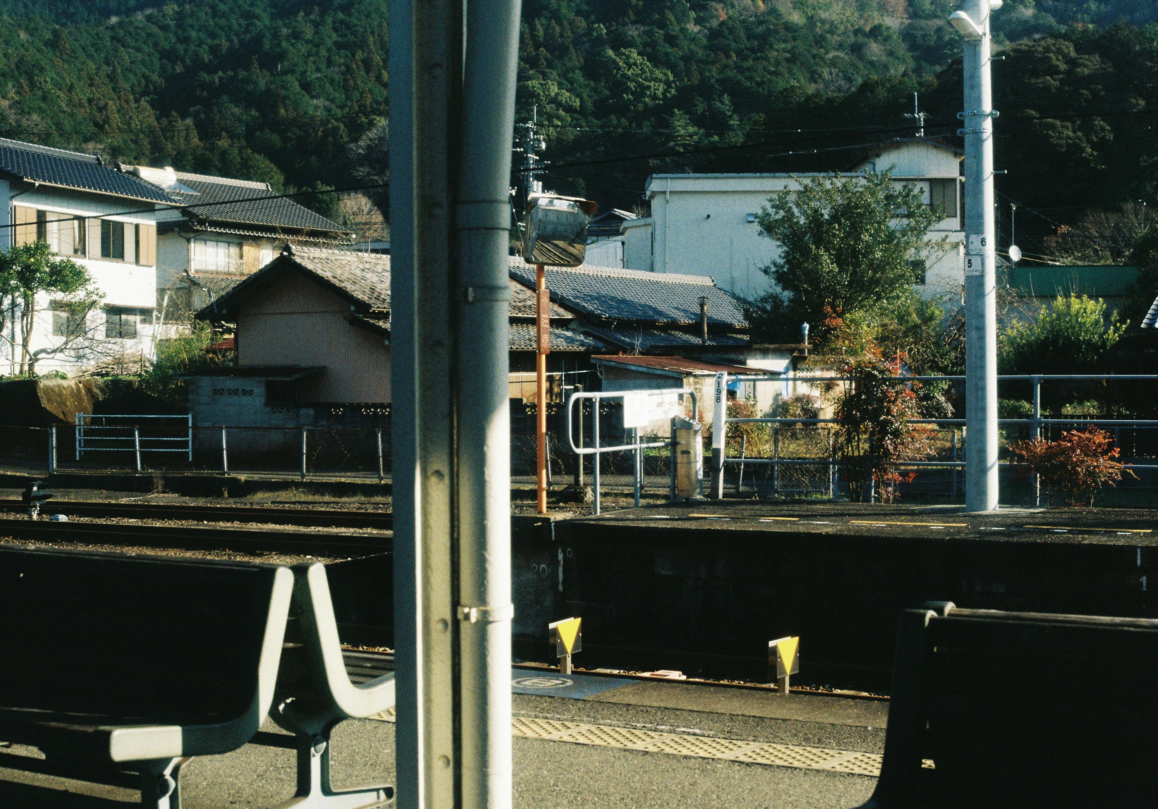 Vista desde el área de espera de una estación de tren con casas antiguas y un fondo montañoso