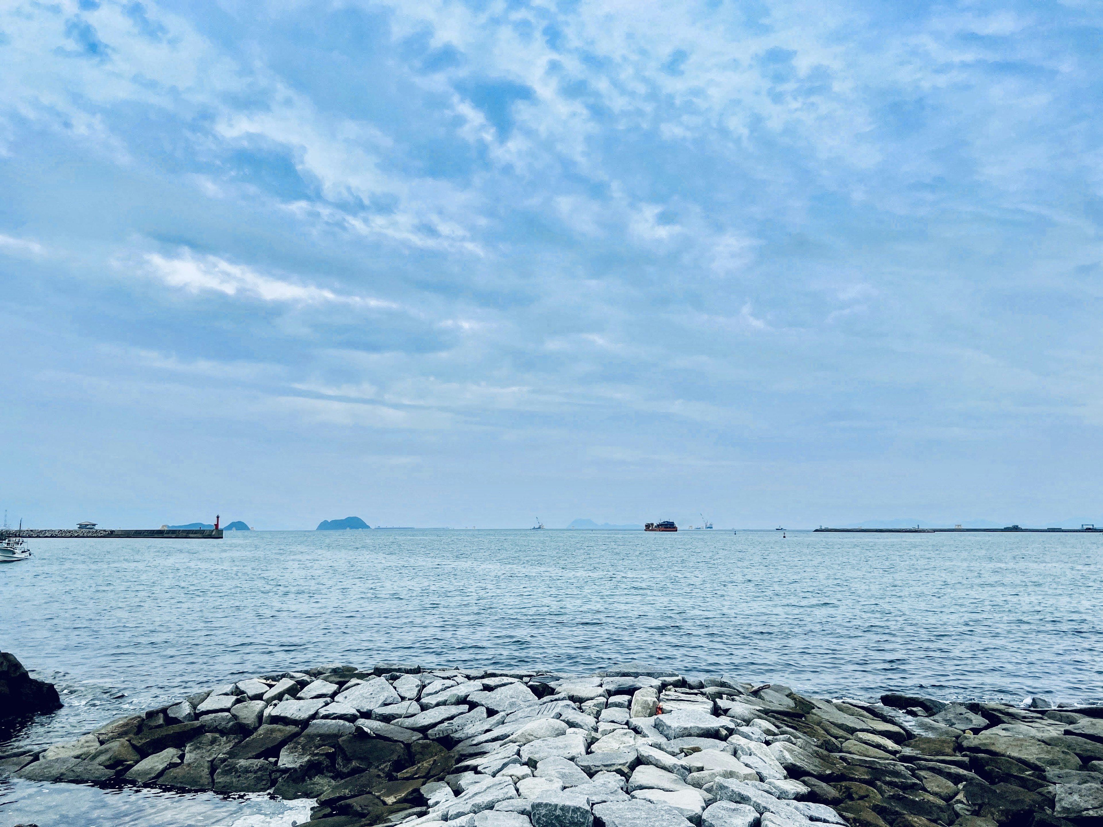 Scenic view of blue sea and sky with a rocky shoreline and distant boats