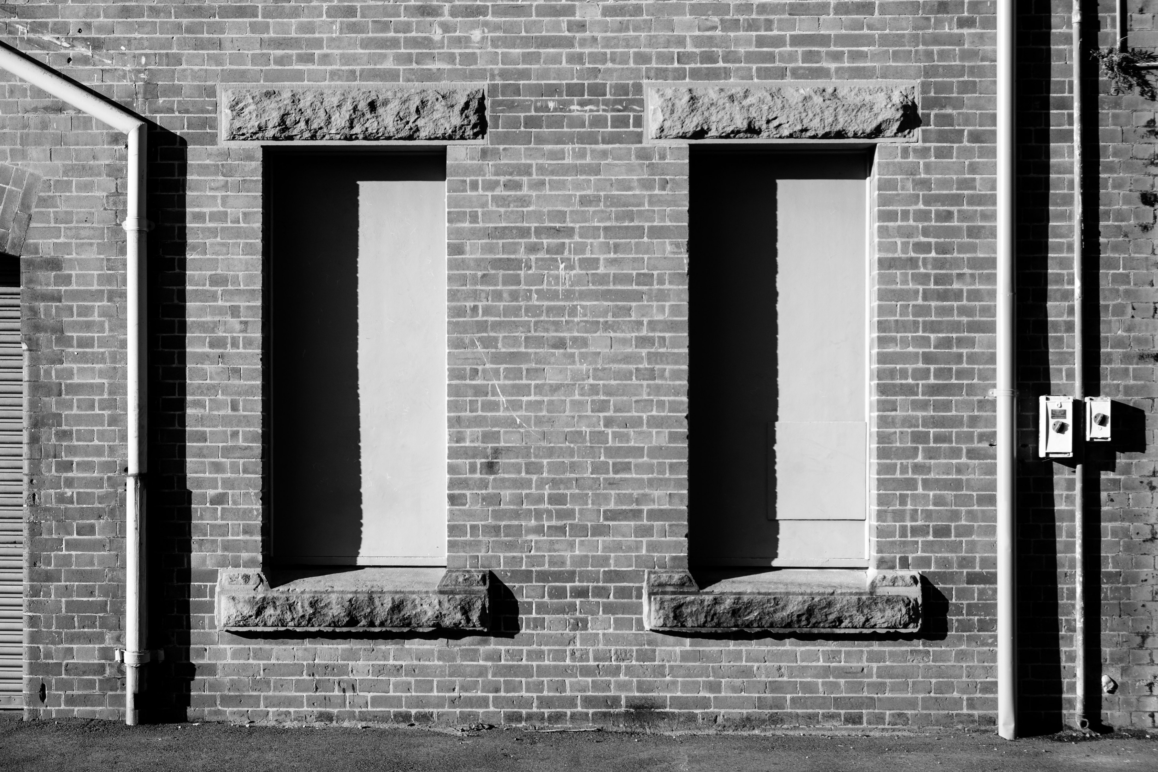 Zwei Fenster mit Steinsimsen an einer Ziegelmauer und Stromzählern