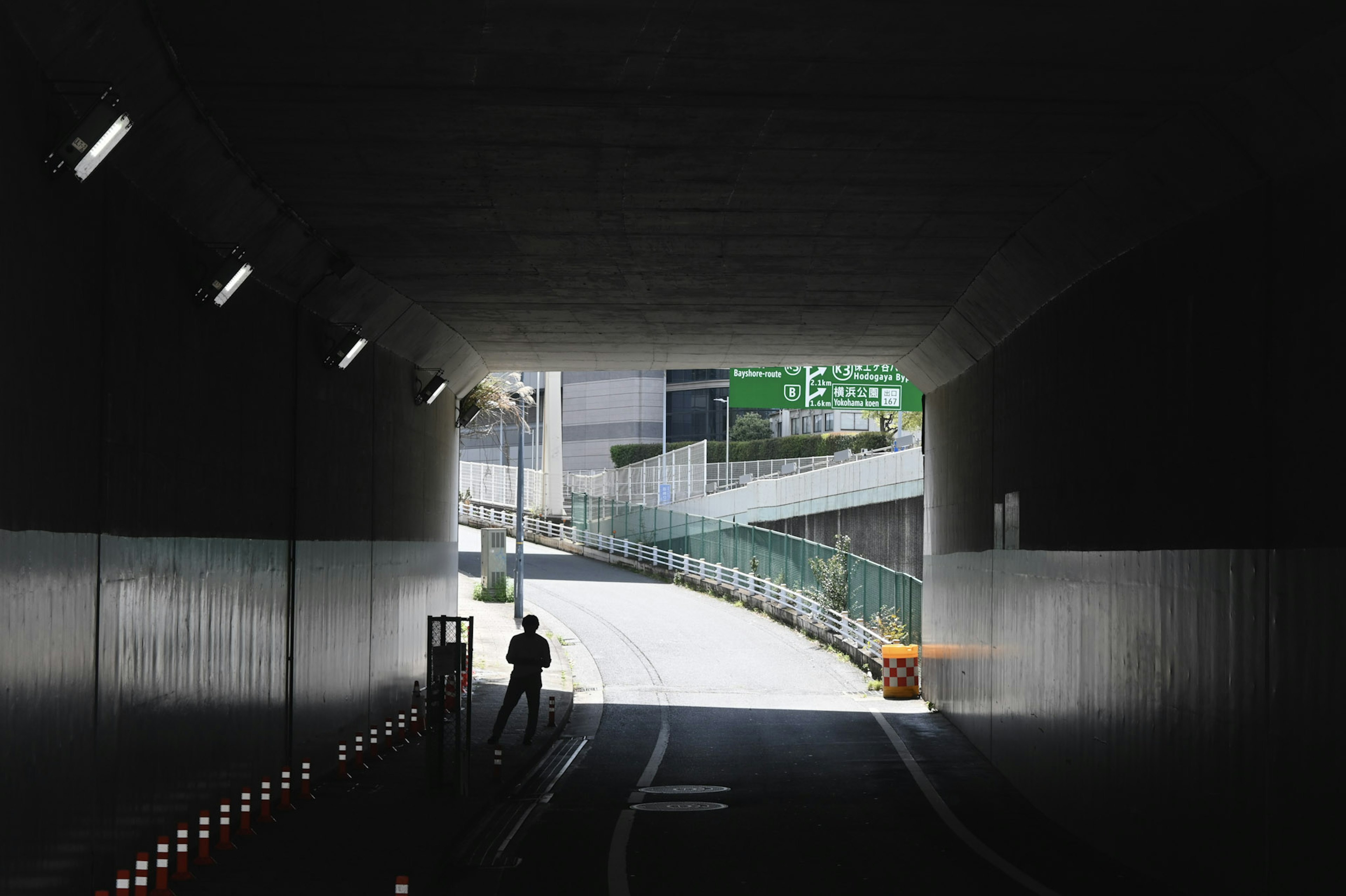 View from inside a tunnel showing a silhouette of a person and traffic signs ahead