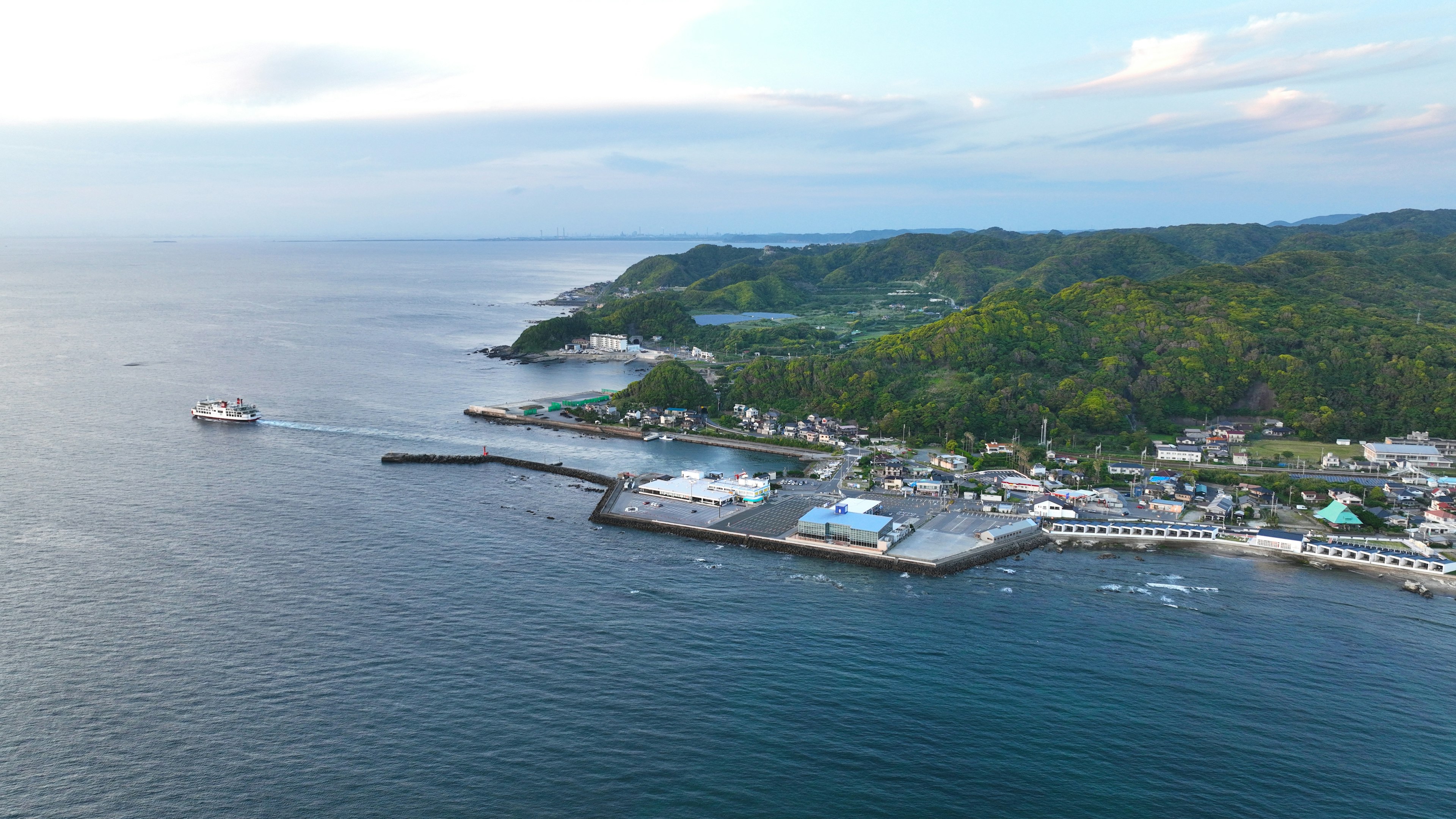 Aerial view of a coastal town featuring a dock with a ferry and lush hills