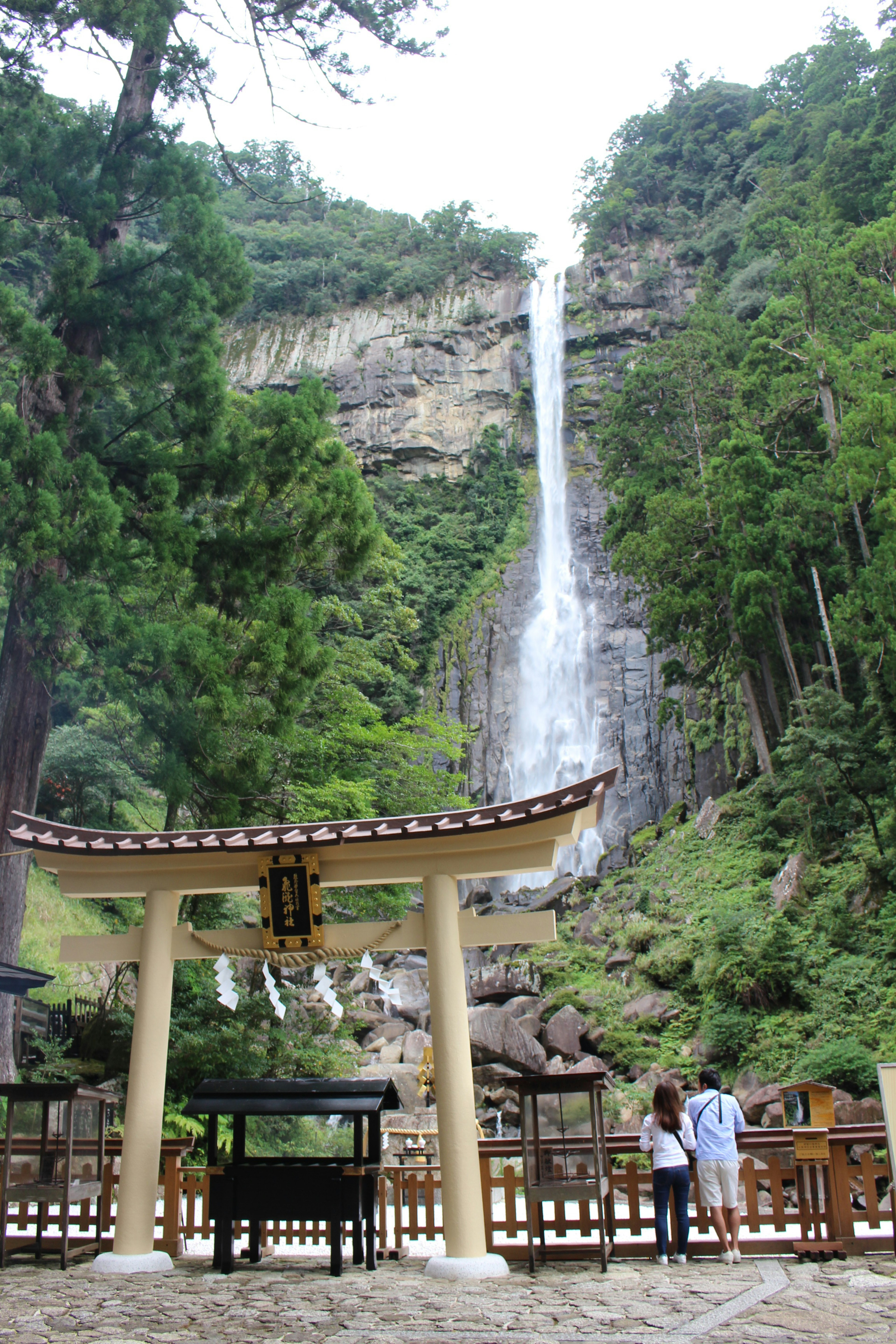 Puerta torii con personas frente a una cascada rodeada de vegetación exuberante