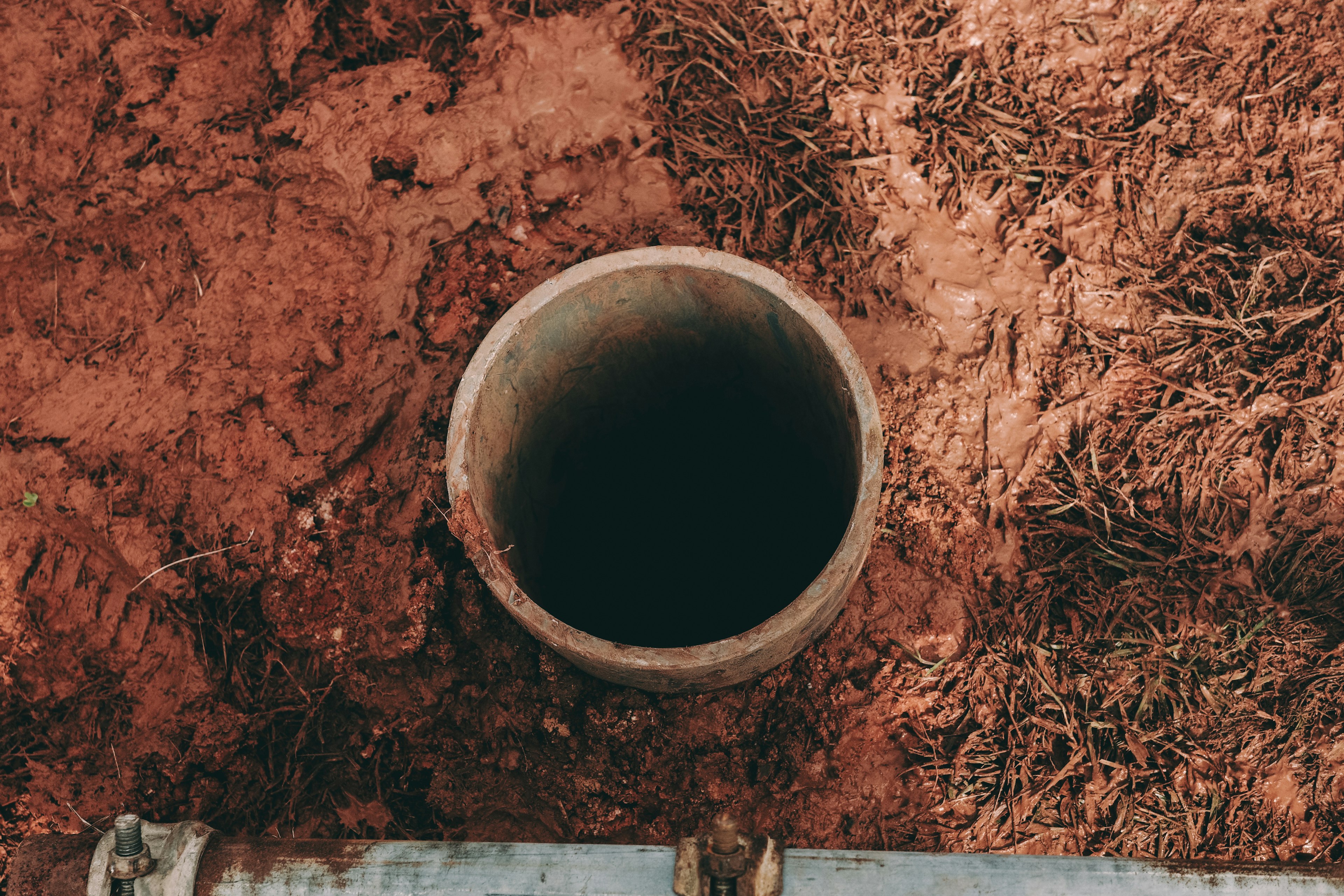 Primo piano di un tubo cilindrico parzialmente sepolto in terreno rossastro