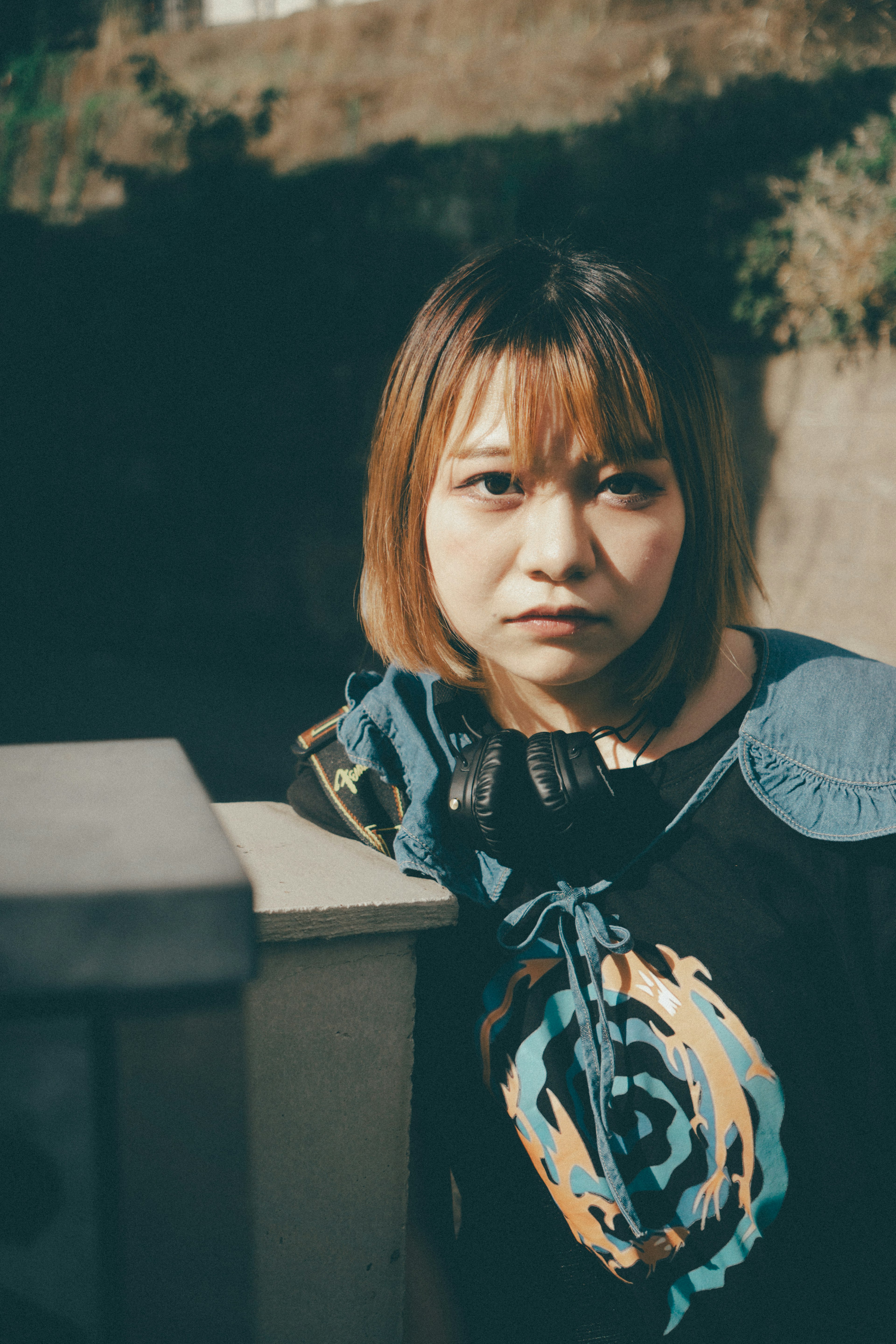 A woman deep in thought by a wall wearing a blue scarf with natural light illuminating her