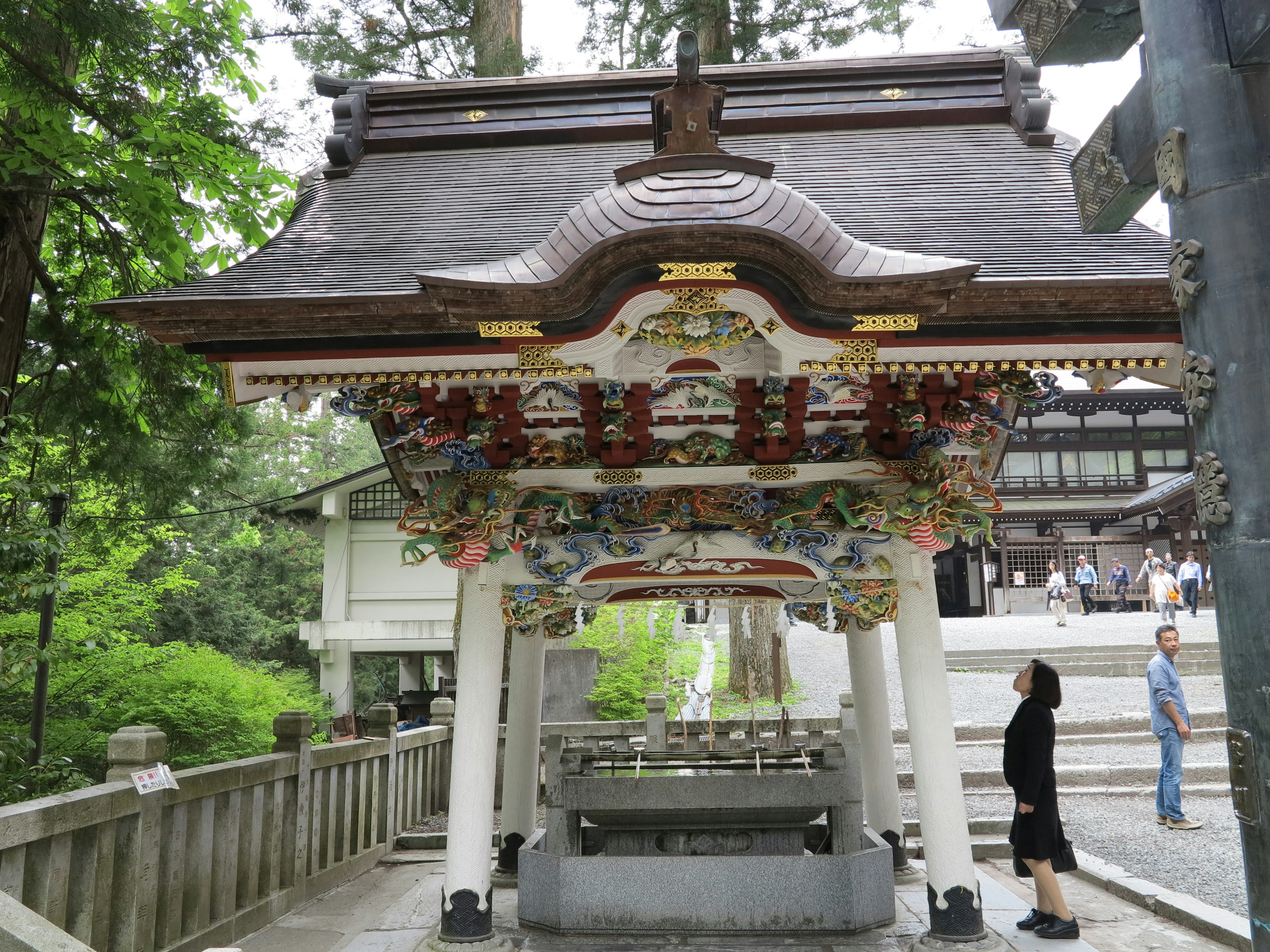 Traditional shrine structure with intricate carvings under the roof featuring visitors