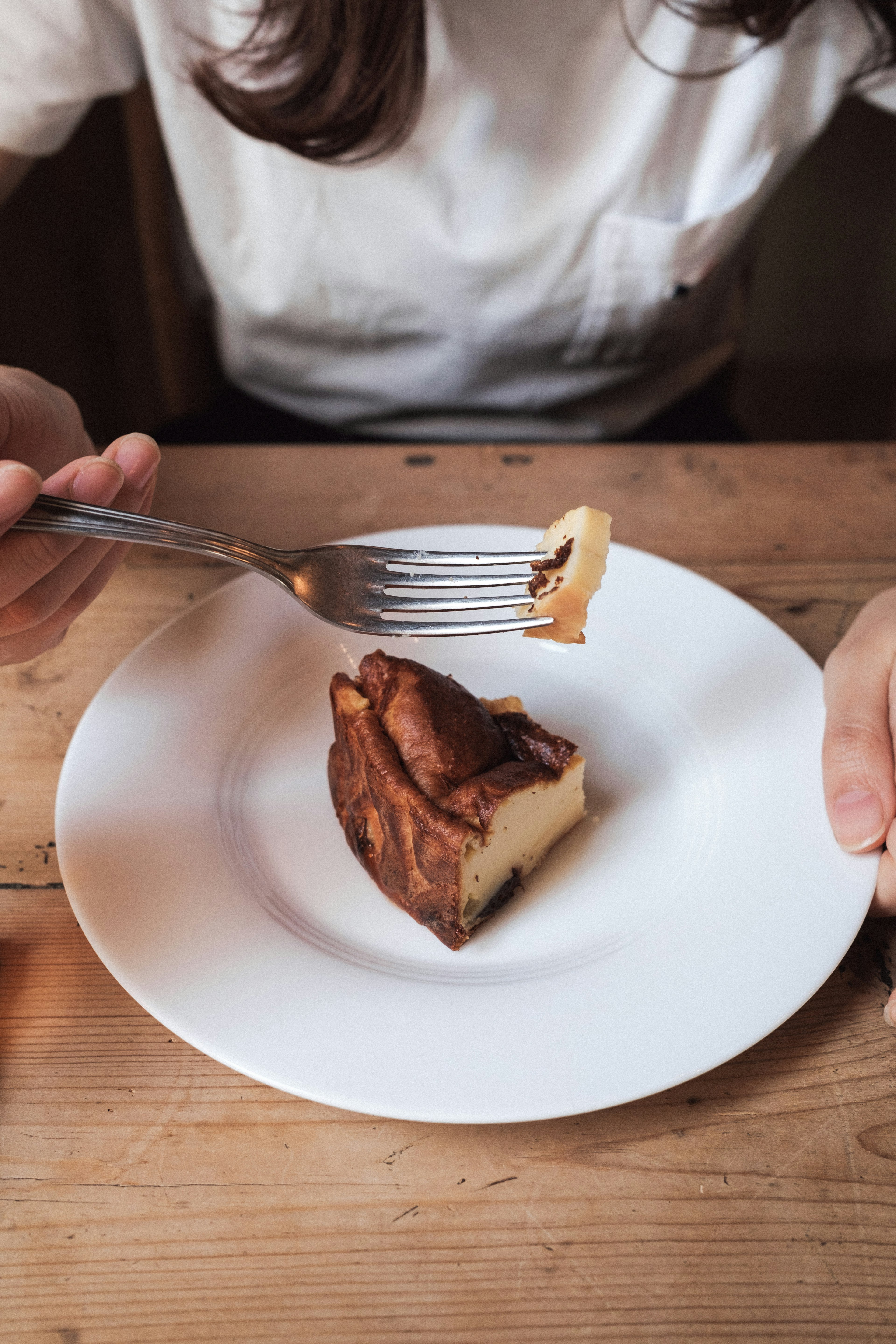 A person's hand holding a fork with a slice of cake on a white plate