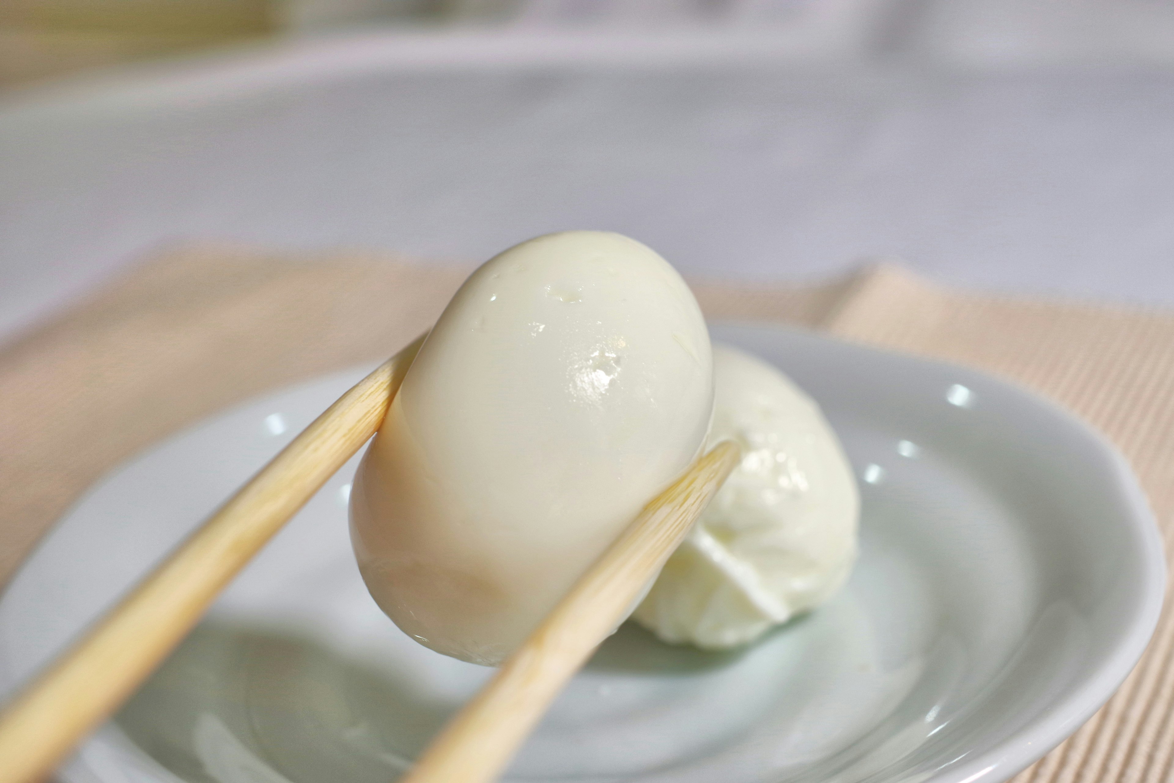 A white egg held by chopsticks on a plate