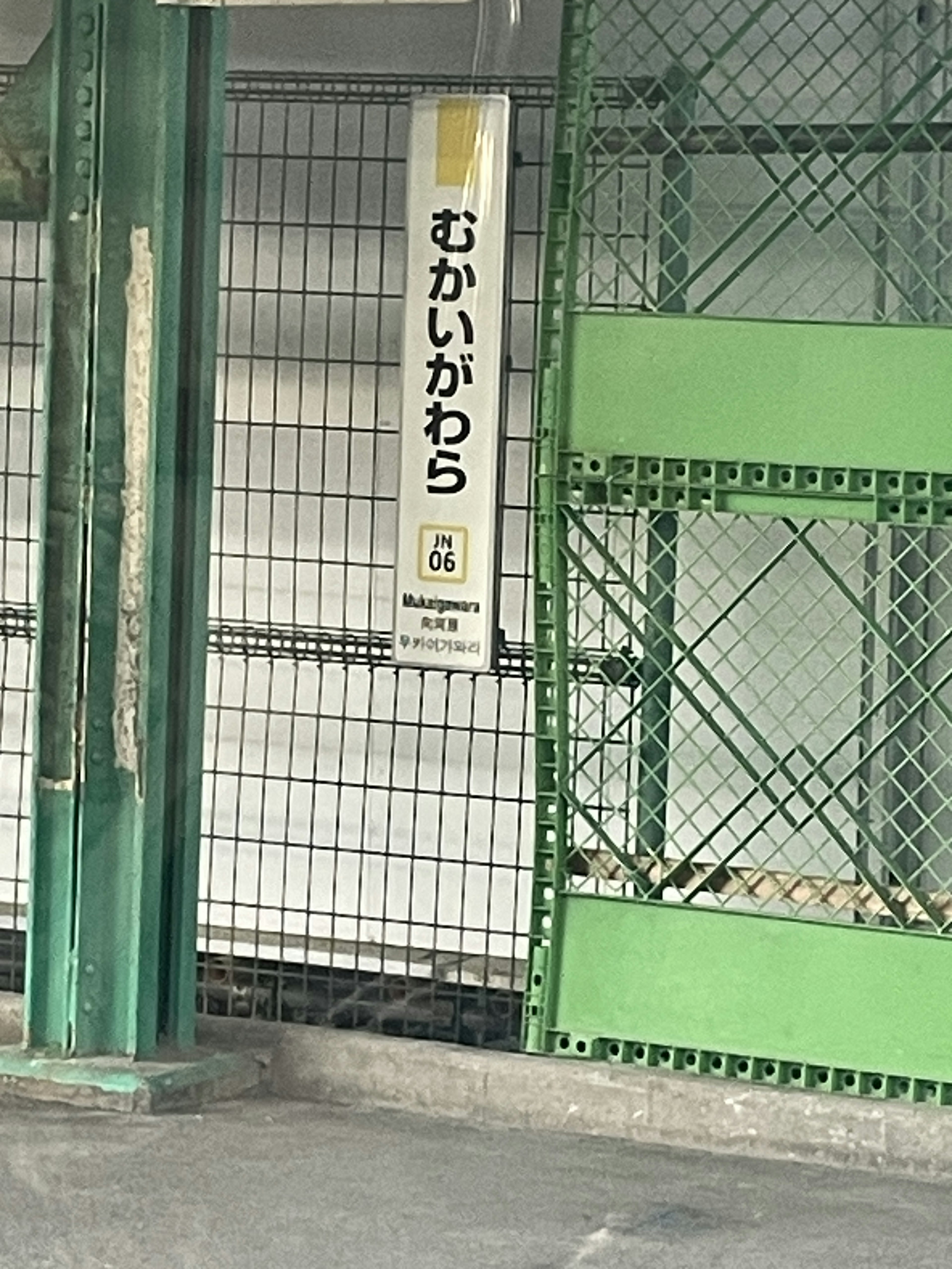 Section of a parking area with a green fence and sign