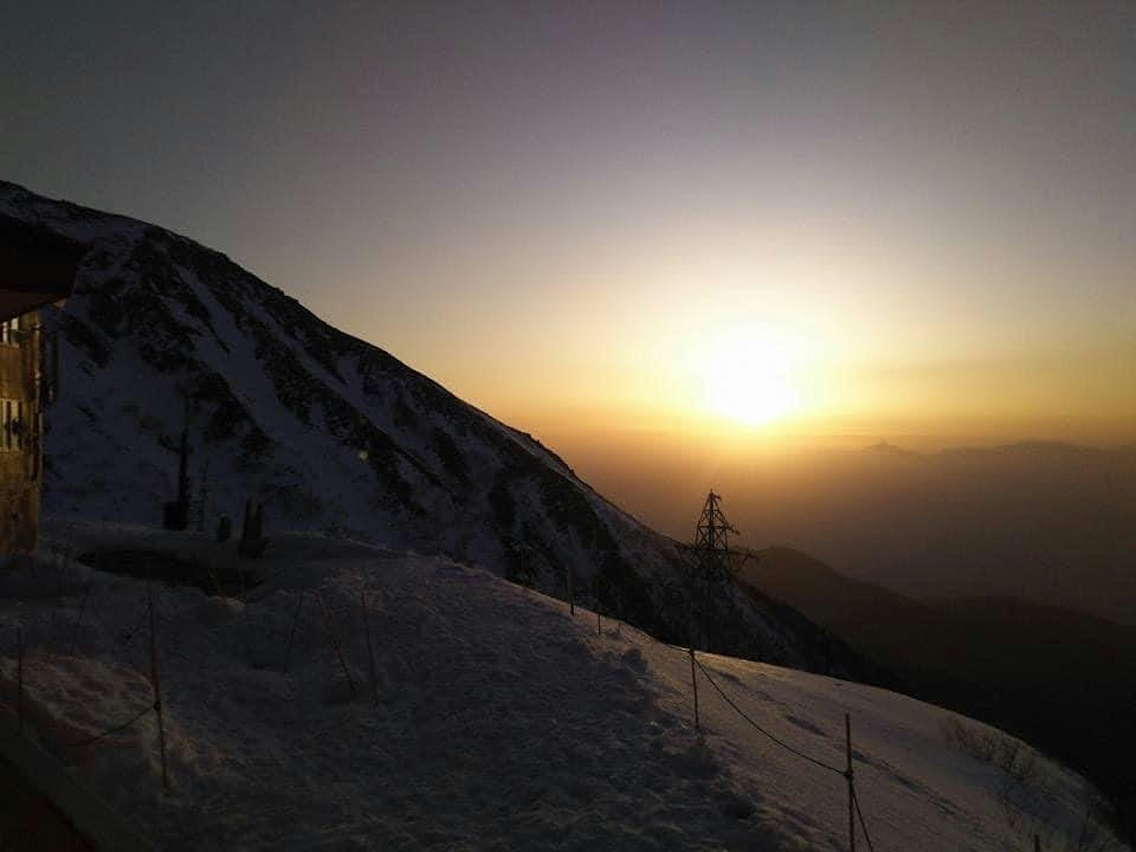 雪に覆われた山の斜面から見える夕日と山のシルエット