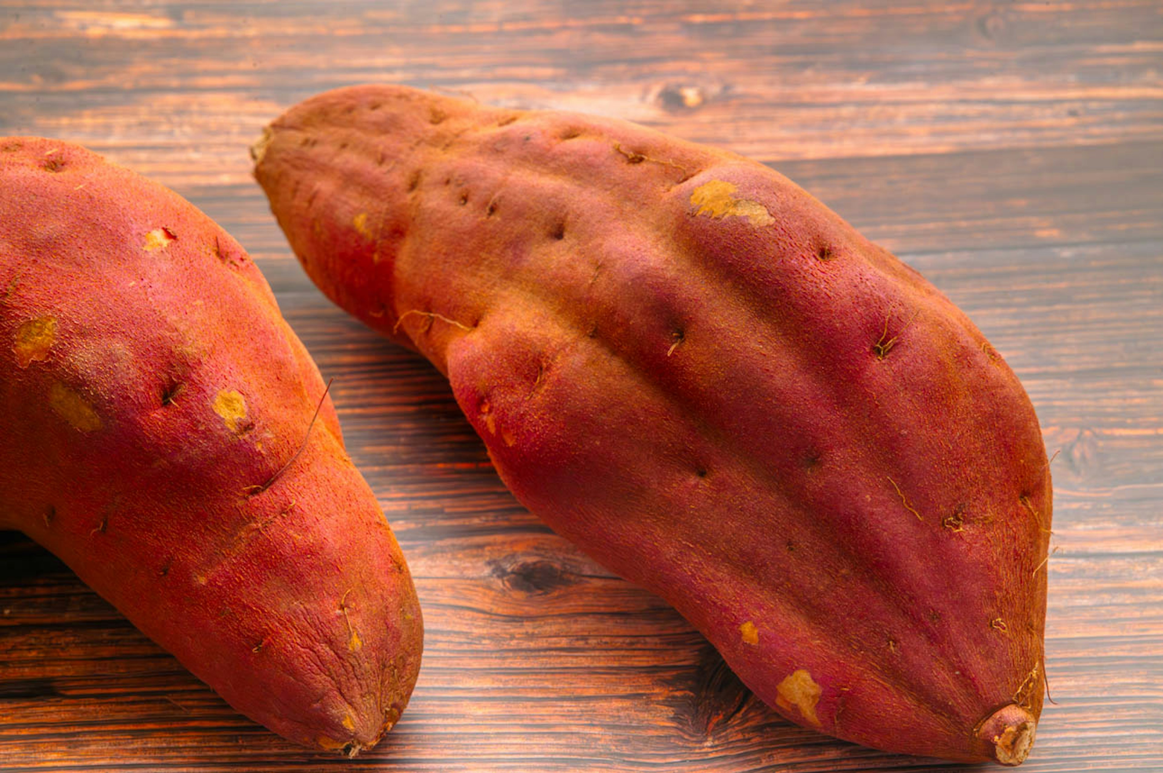 Two red sweet potatoes on a wooden table