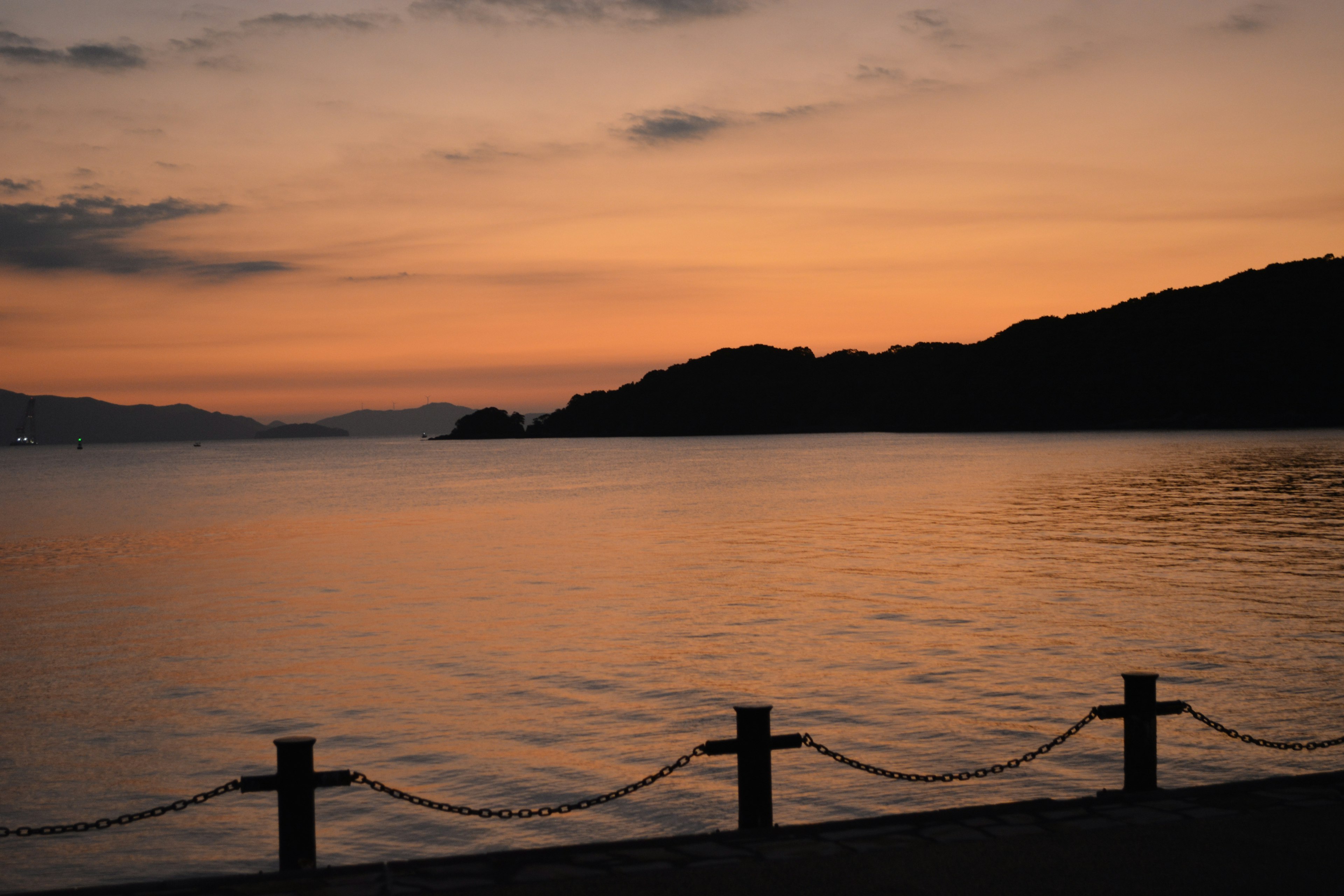 夕焼けの海と島々の景色、穏やかな水面、ボードウォークに沿ったロープ