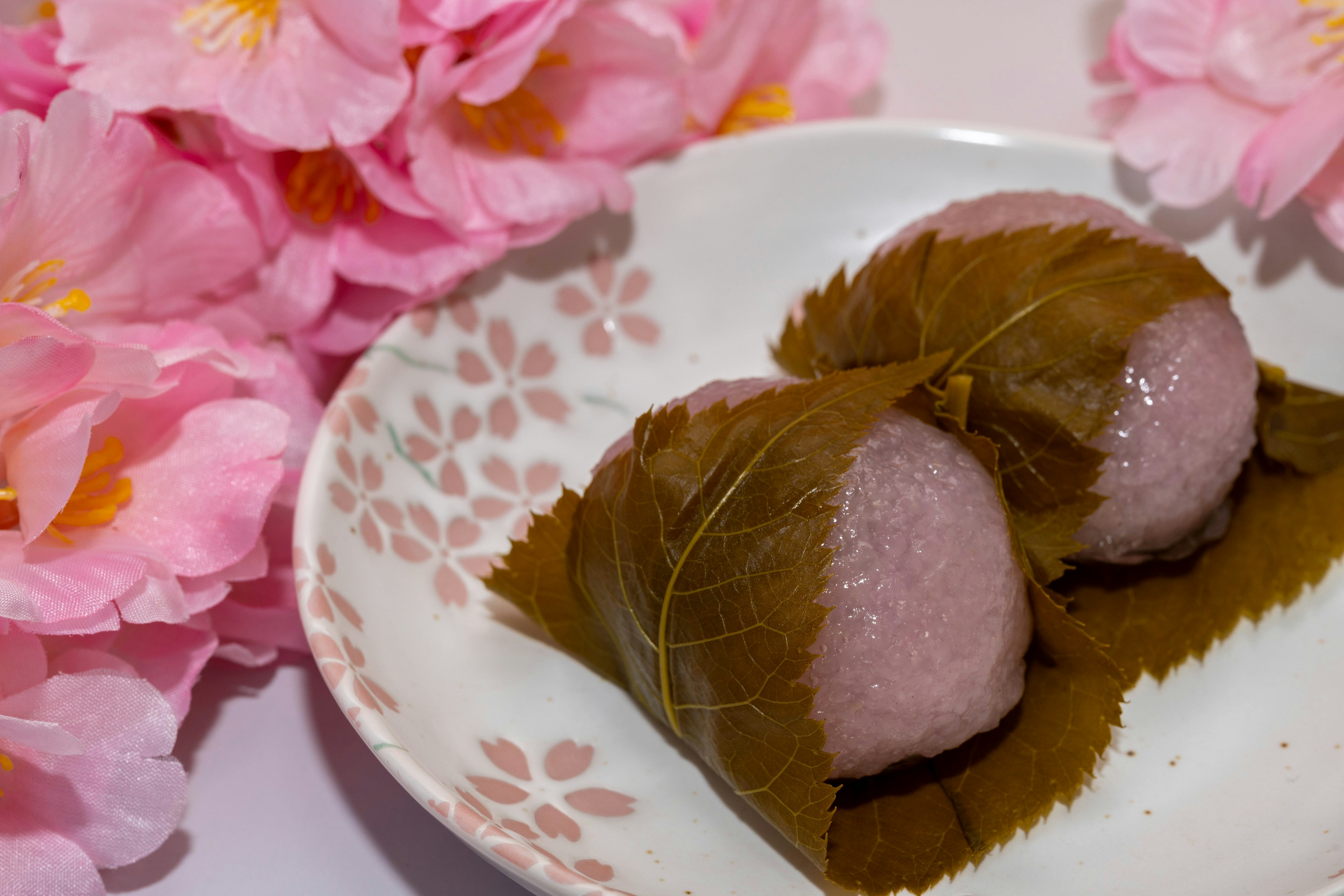 Sakura-Mochi auf einem dekorativen Teller mit Kirschblüten-Hintergrund