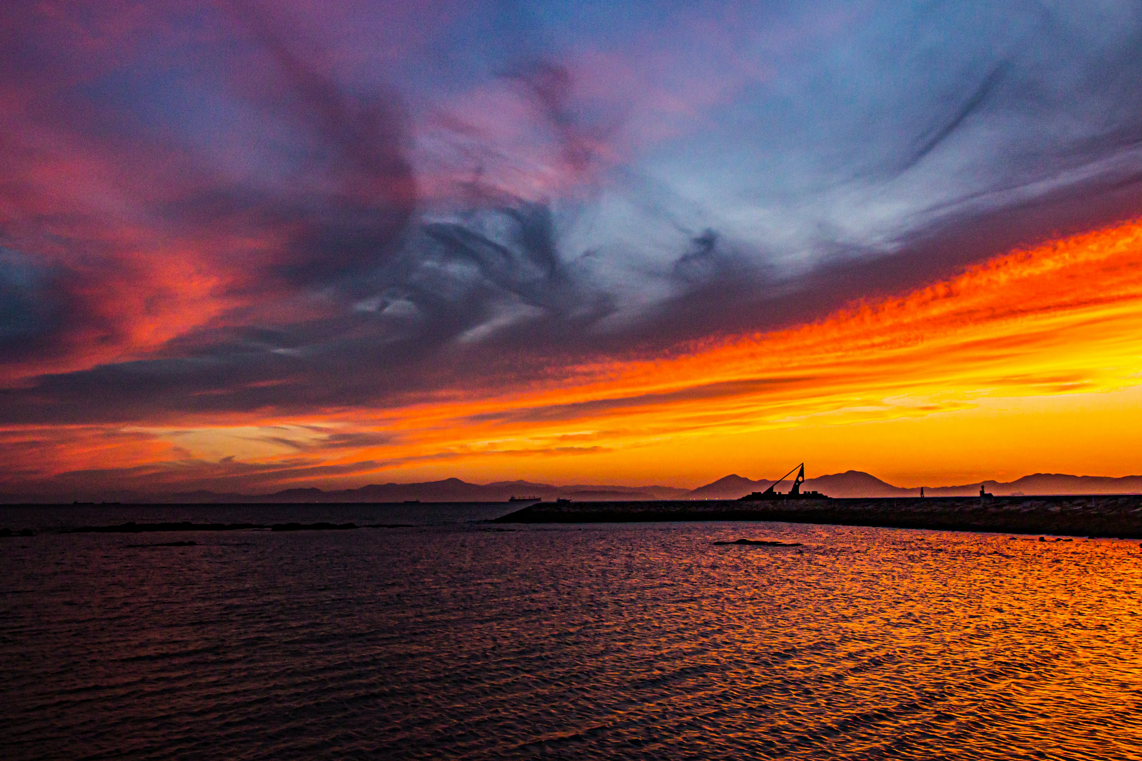 Senja yang cerah di atas lautan dengan pegunungan di kejauhan