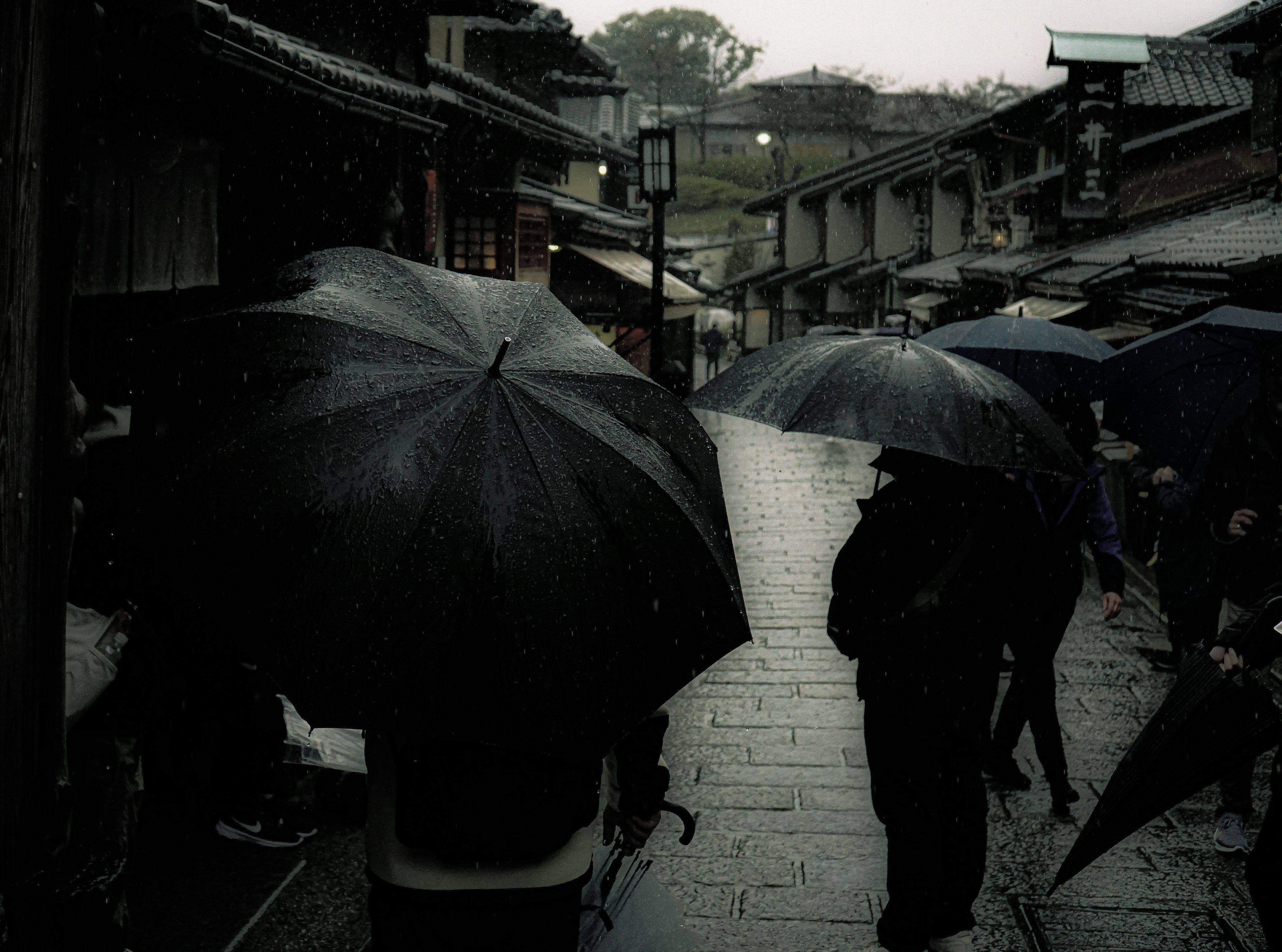 People with umbrellas walking in the rain along an old street