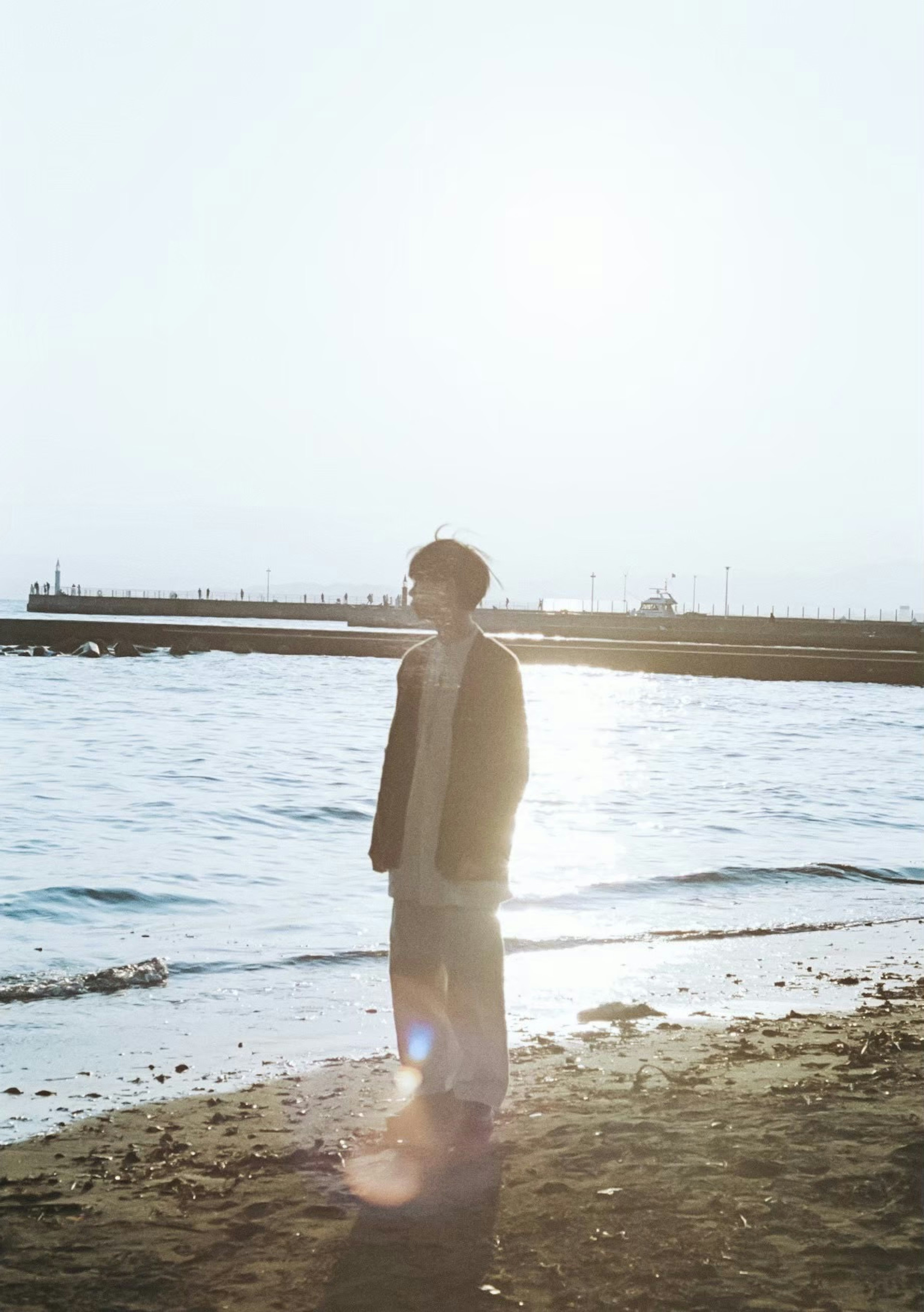 Silhouette of a person standing by the beach Sunlight reflecting on the water sandy shore