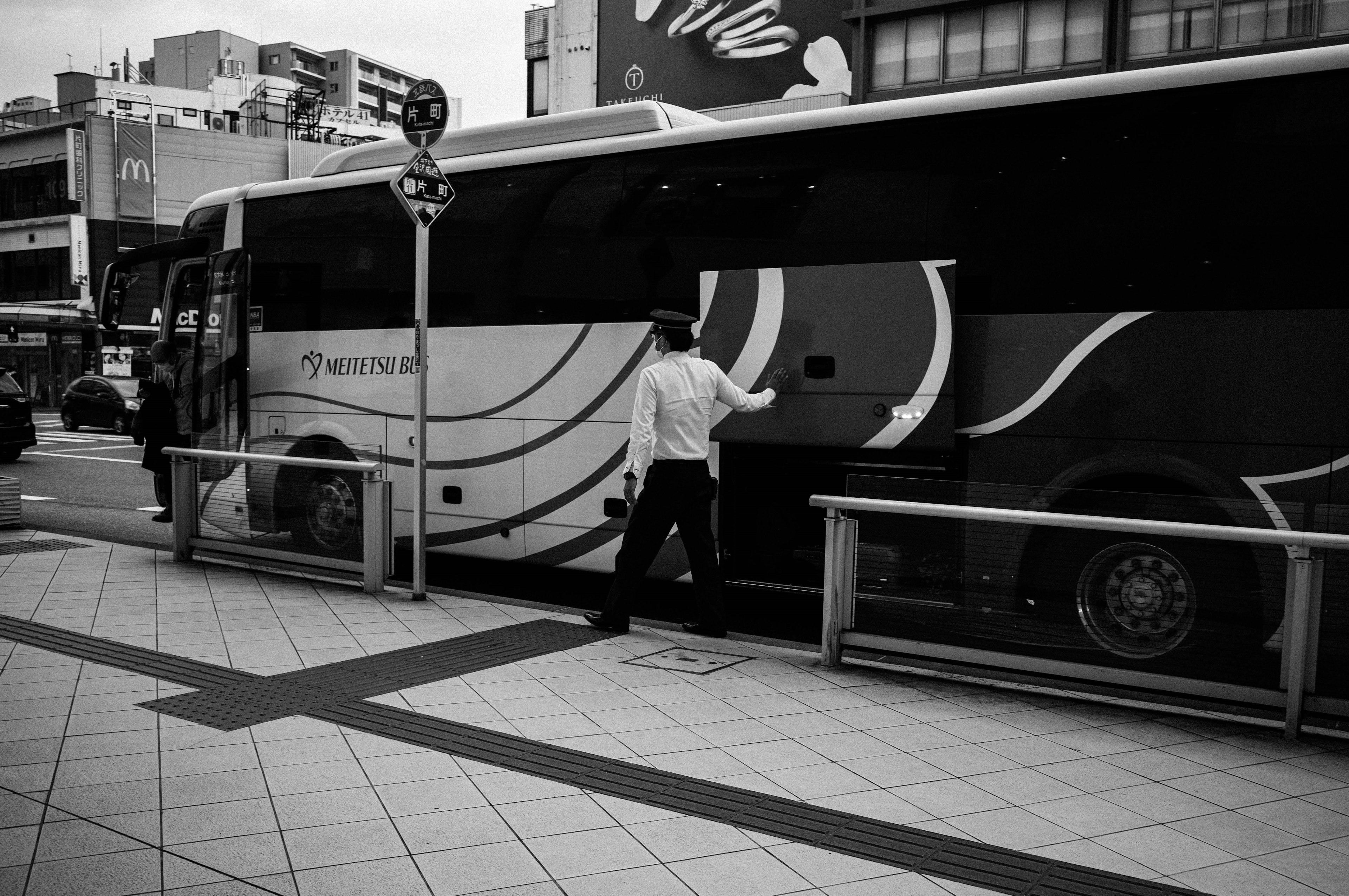 Schwarzweißfoto einer Person, die an einer Haltestelle in einen Bus einsteigt