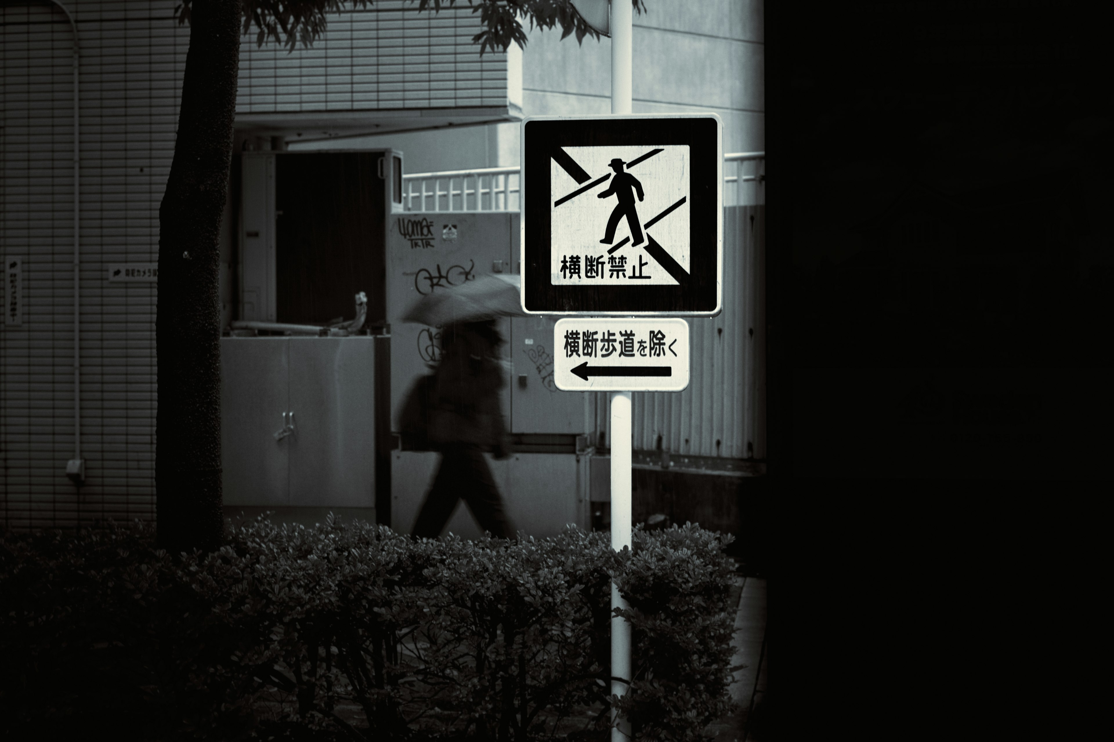 Silhouette of a person walking with an umbrella near a traffic sign