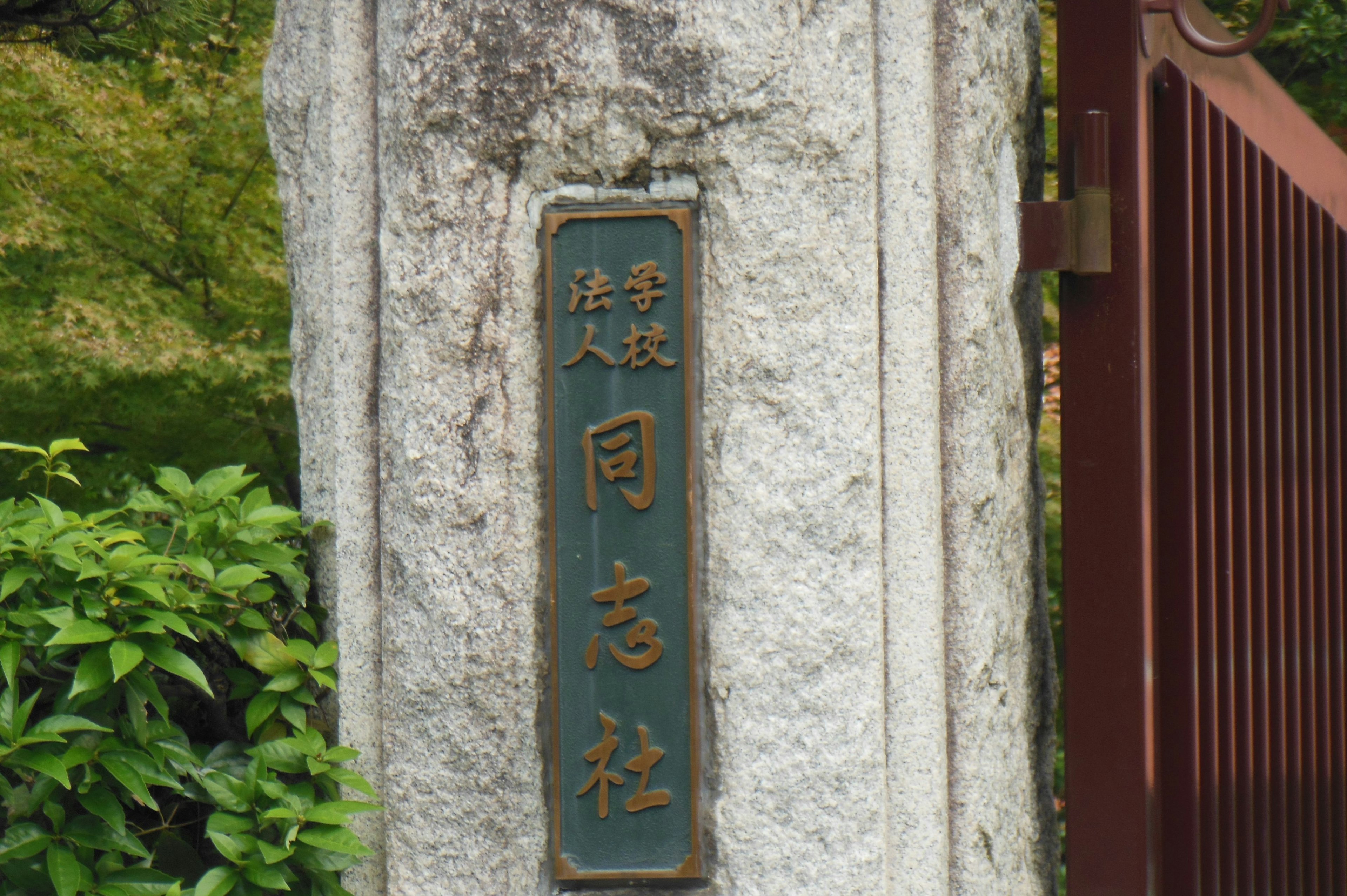 A blue metal plaque with engraved kanji characters on a stone pillar