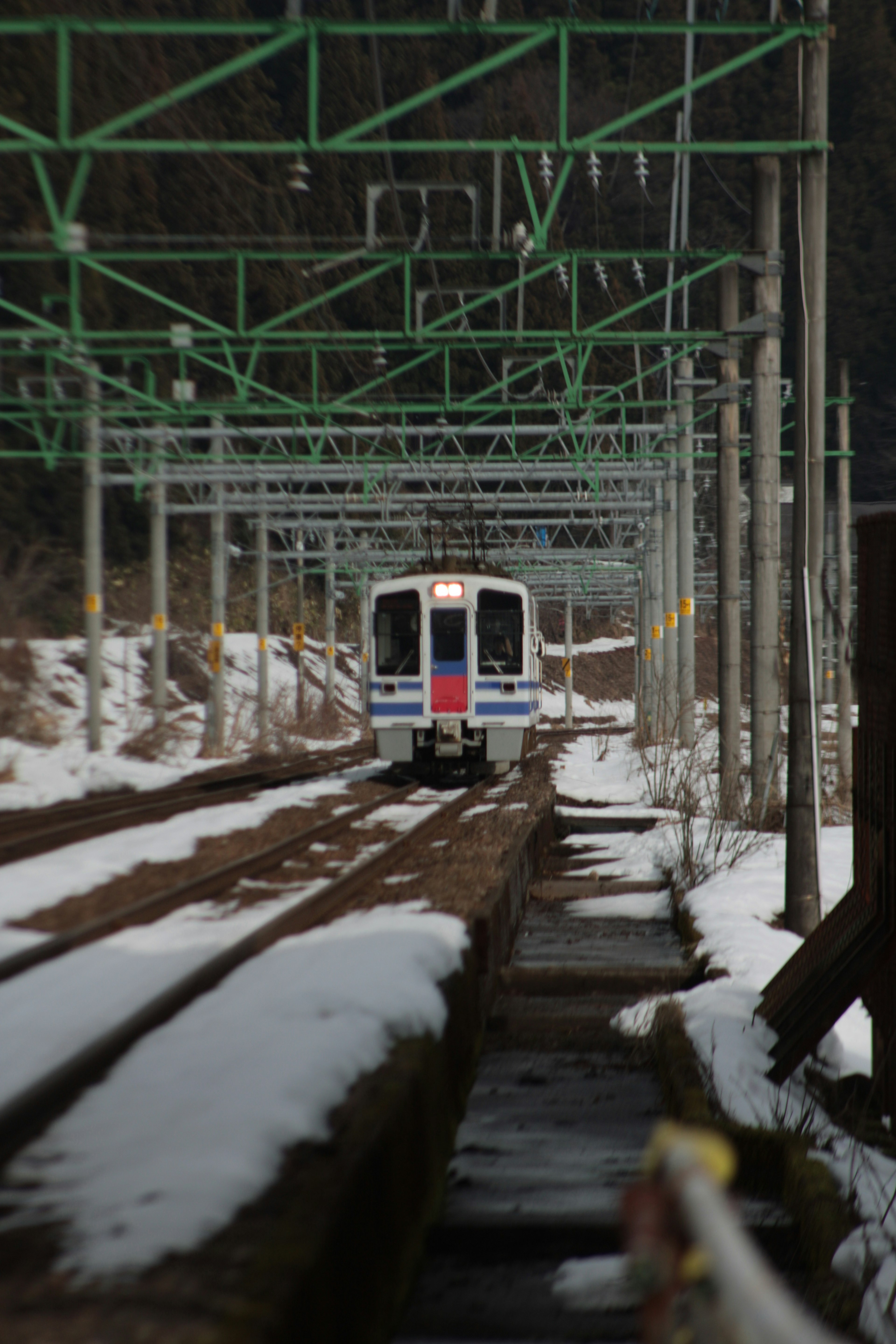 Train on snow-covered tracks under green overhead wires