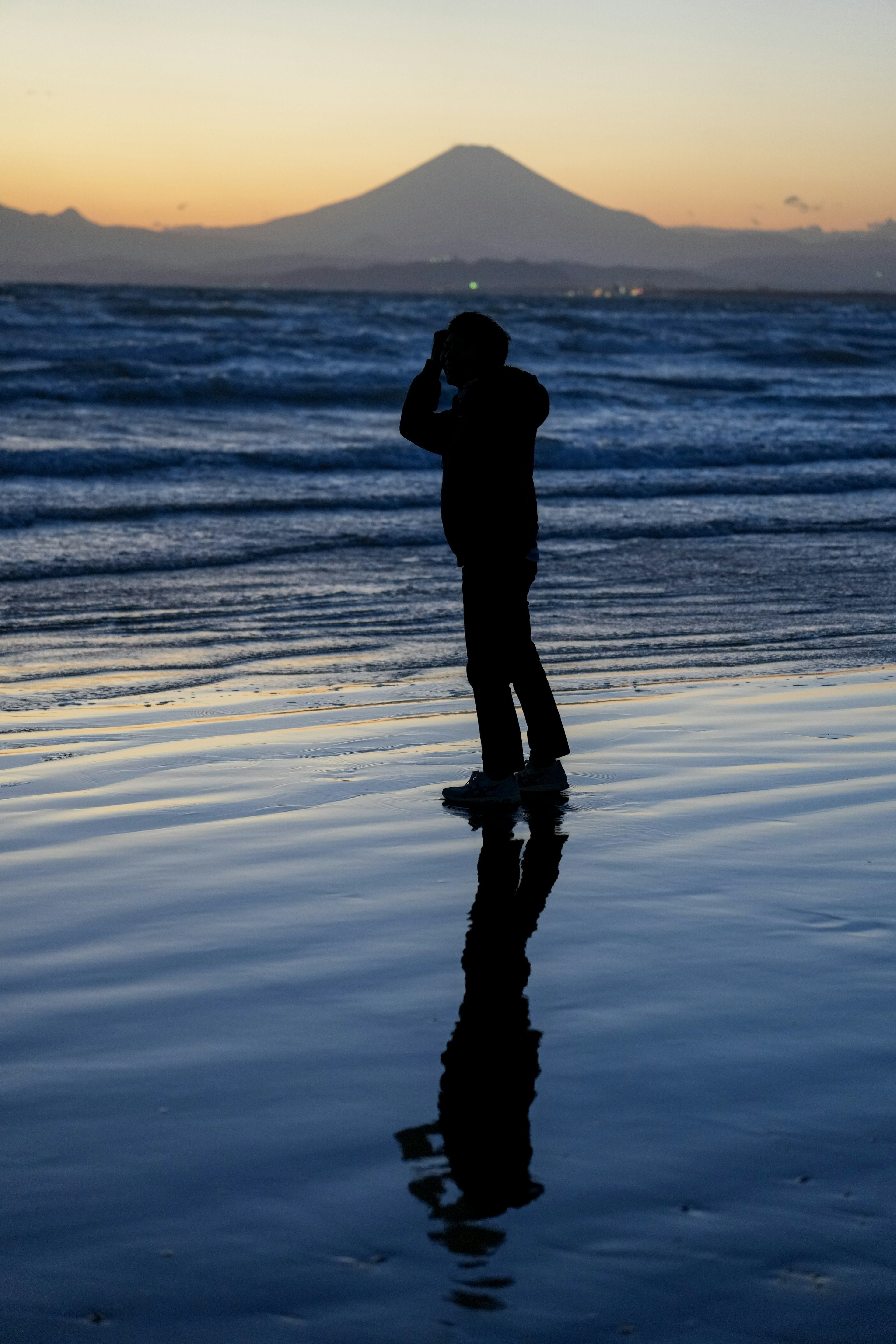 Silueta de una persona en la playa con el Monte Fuji al fondo durante el atardecer