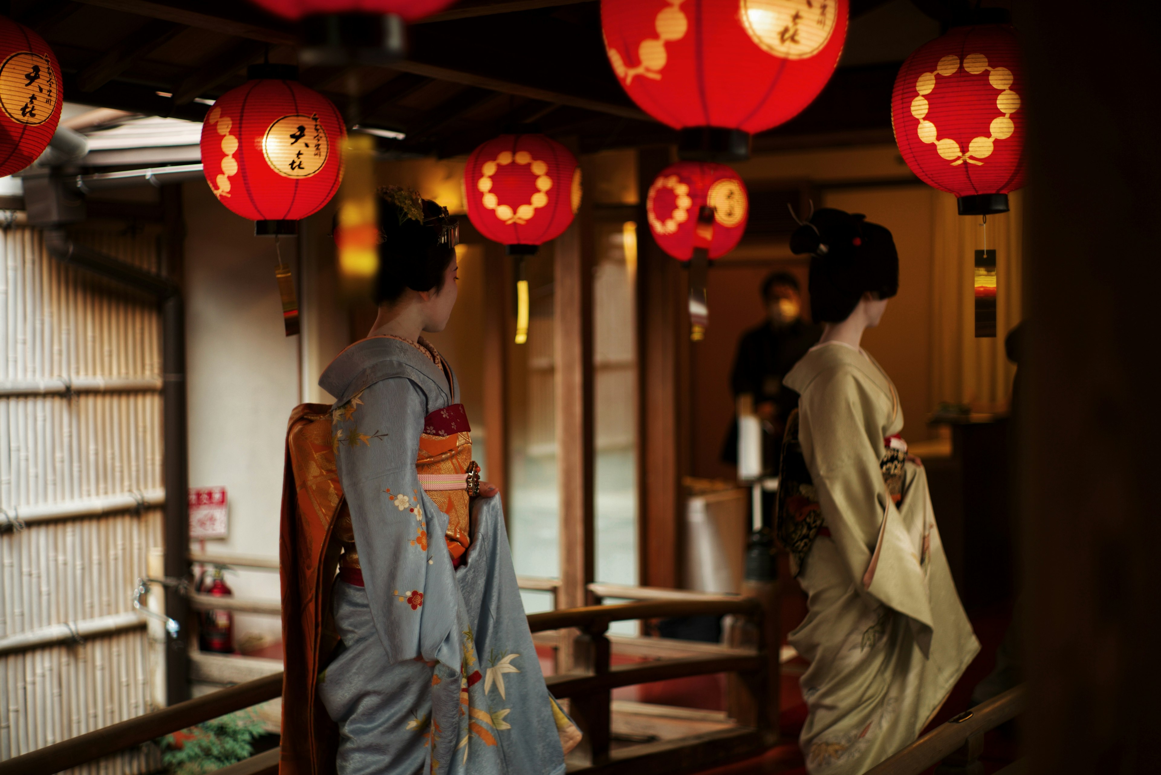 Two women in kimonos standing under red lanterns in a traditional setting