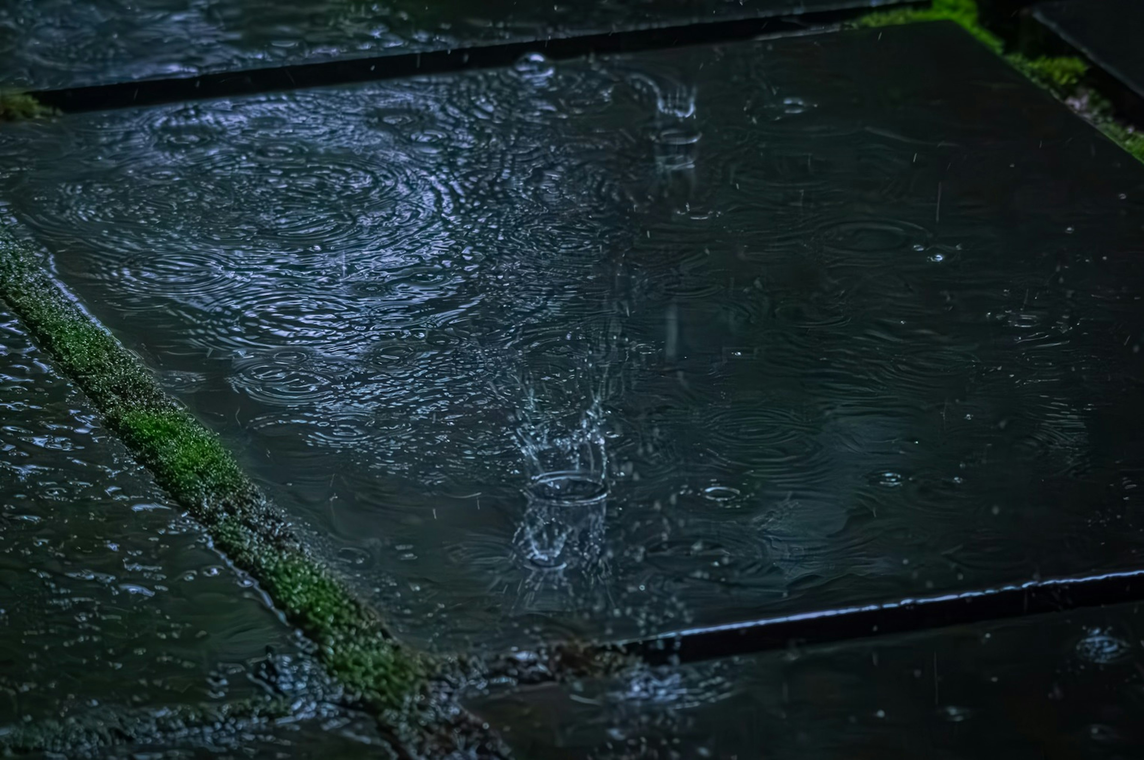 Rain falling on wet stone pavement creating ripples in puddles