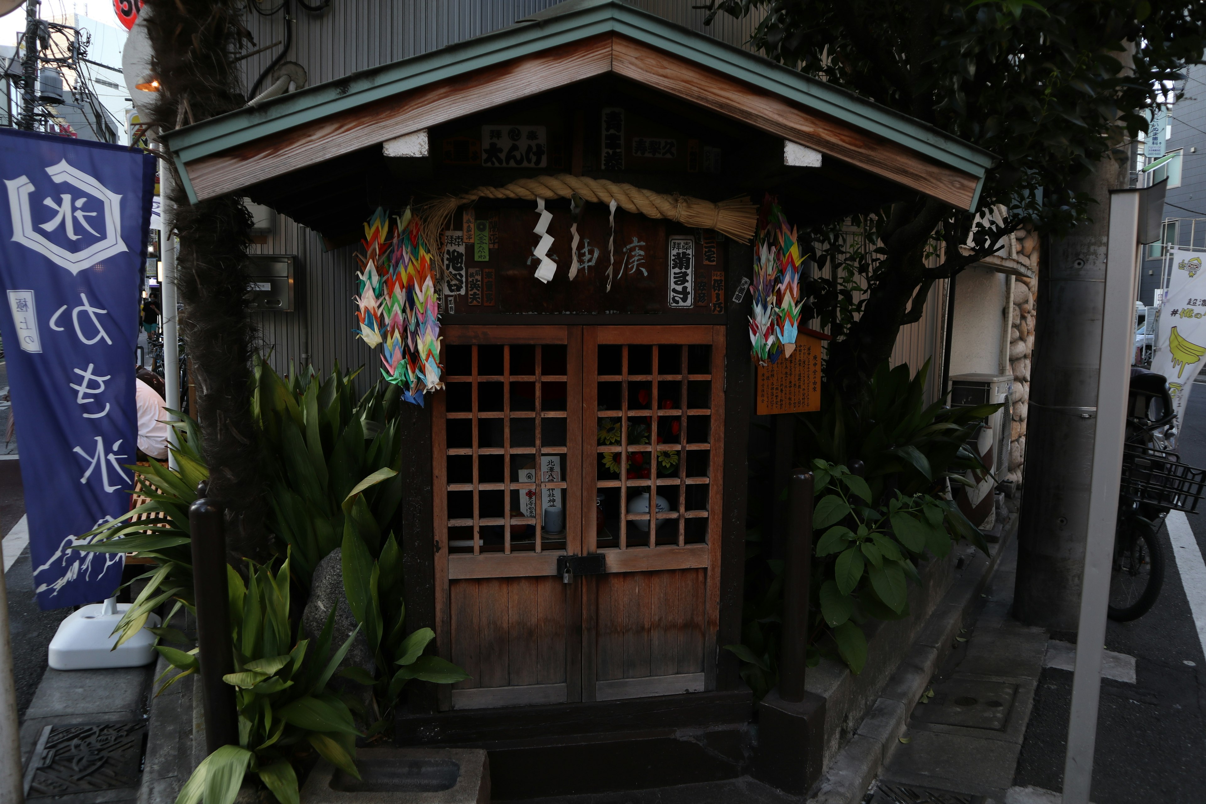 Cabina de santuario japonés tradicional con entrada de madera rodeada de vegetación exuberante y decoraciones coloridas