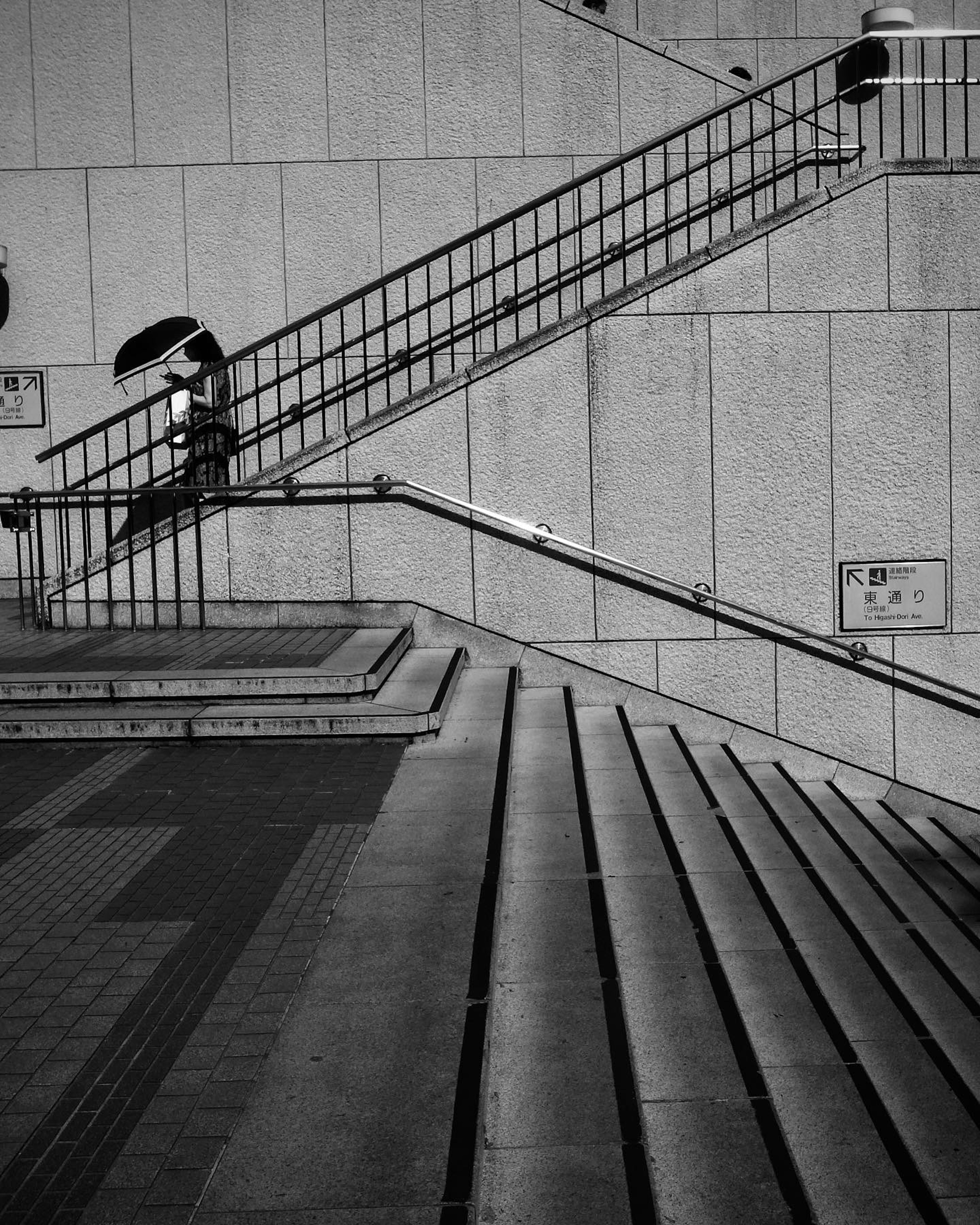 Black and white photo of stairs and railing a person holding an umbrella