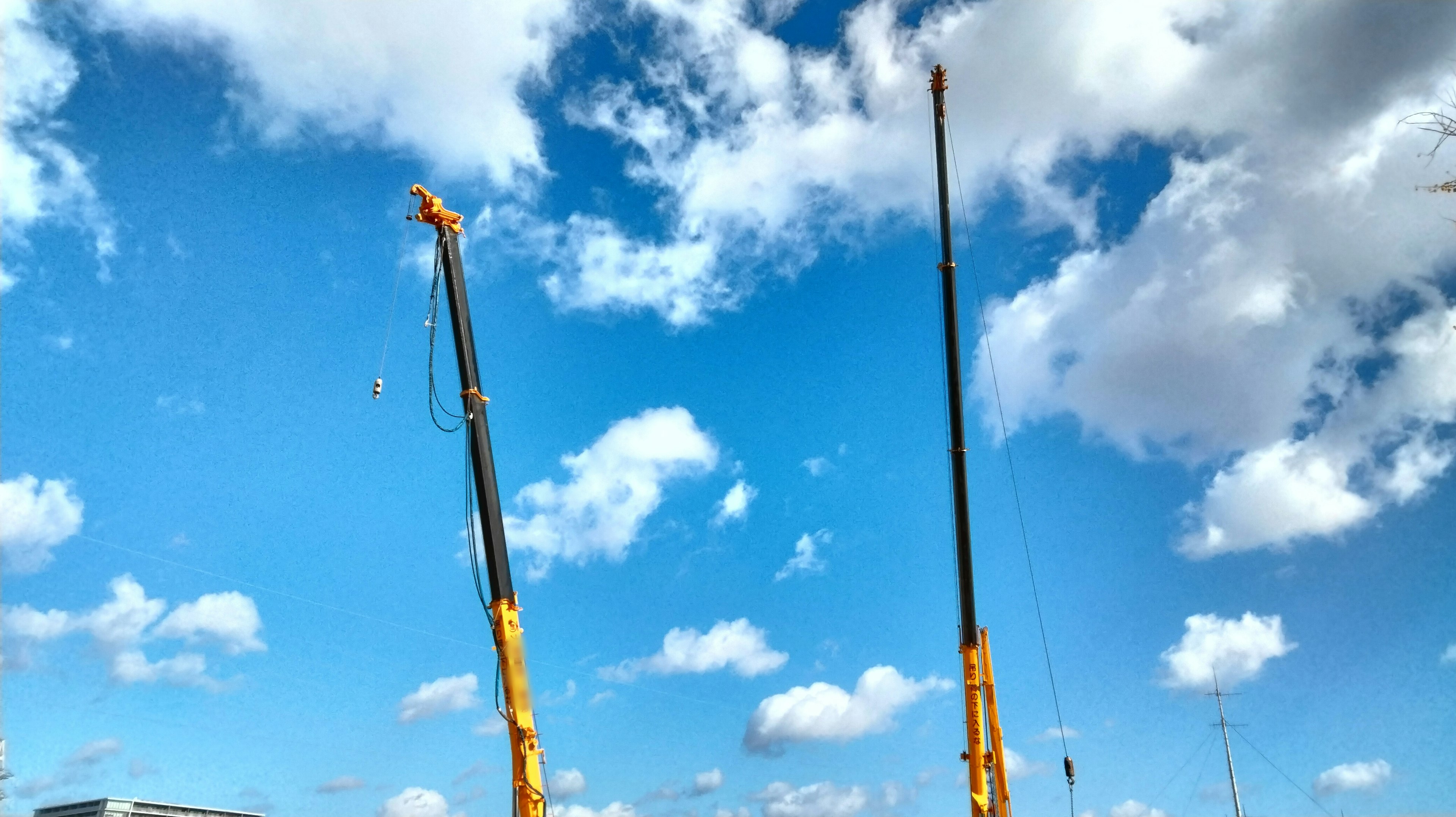 Tall crane arms against a blue sky with clouds