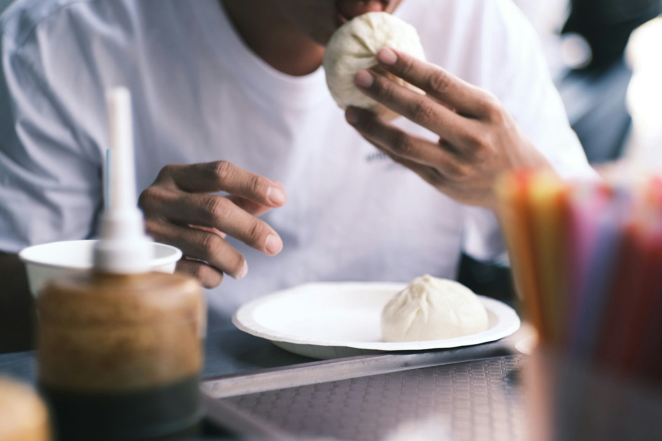 Một người đàn ông đang ăn một chiếc bánh bao trắng cầm chiếc bánh bao trên tay và một chiếc bánh bao khác trên đĩa
