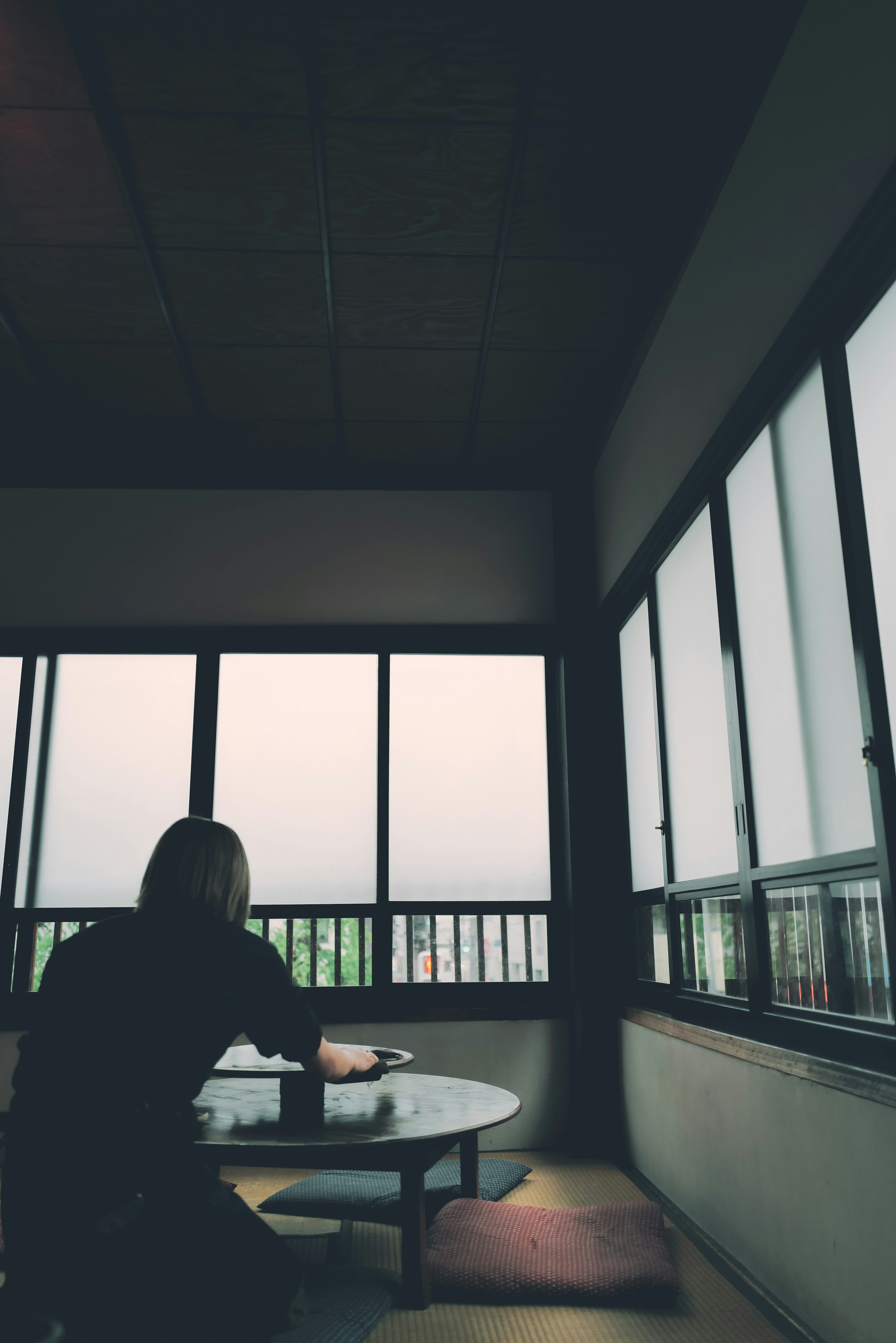 Person sitting by the window in a quiet room with their back turned resting hands on the table