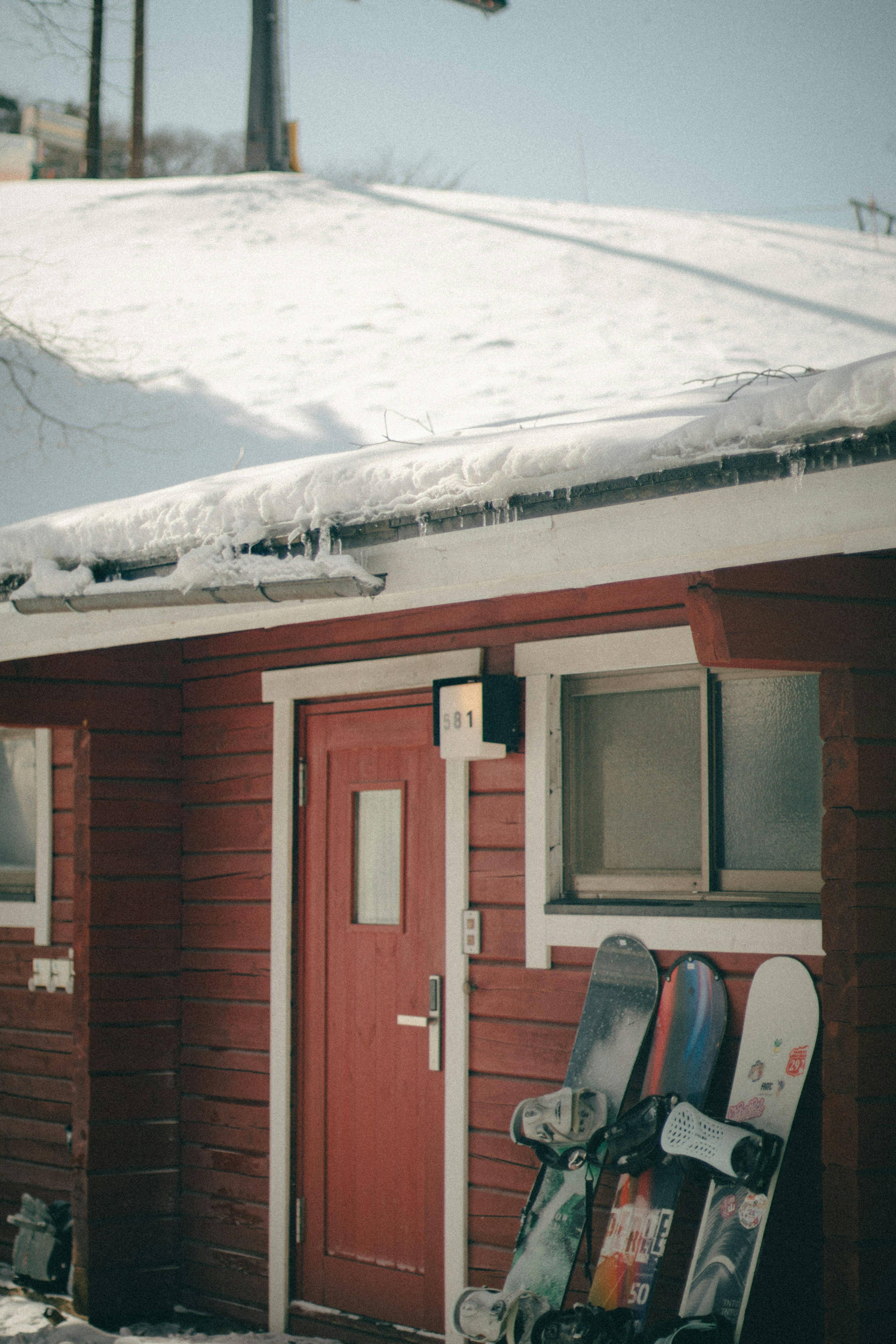 Snowy scene with a red cabin and snowboards by the door