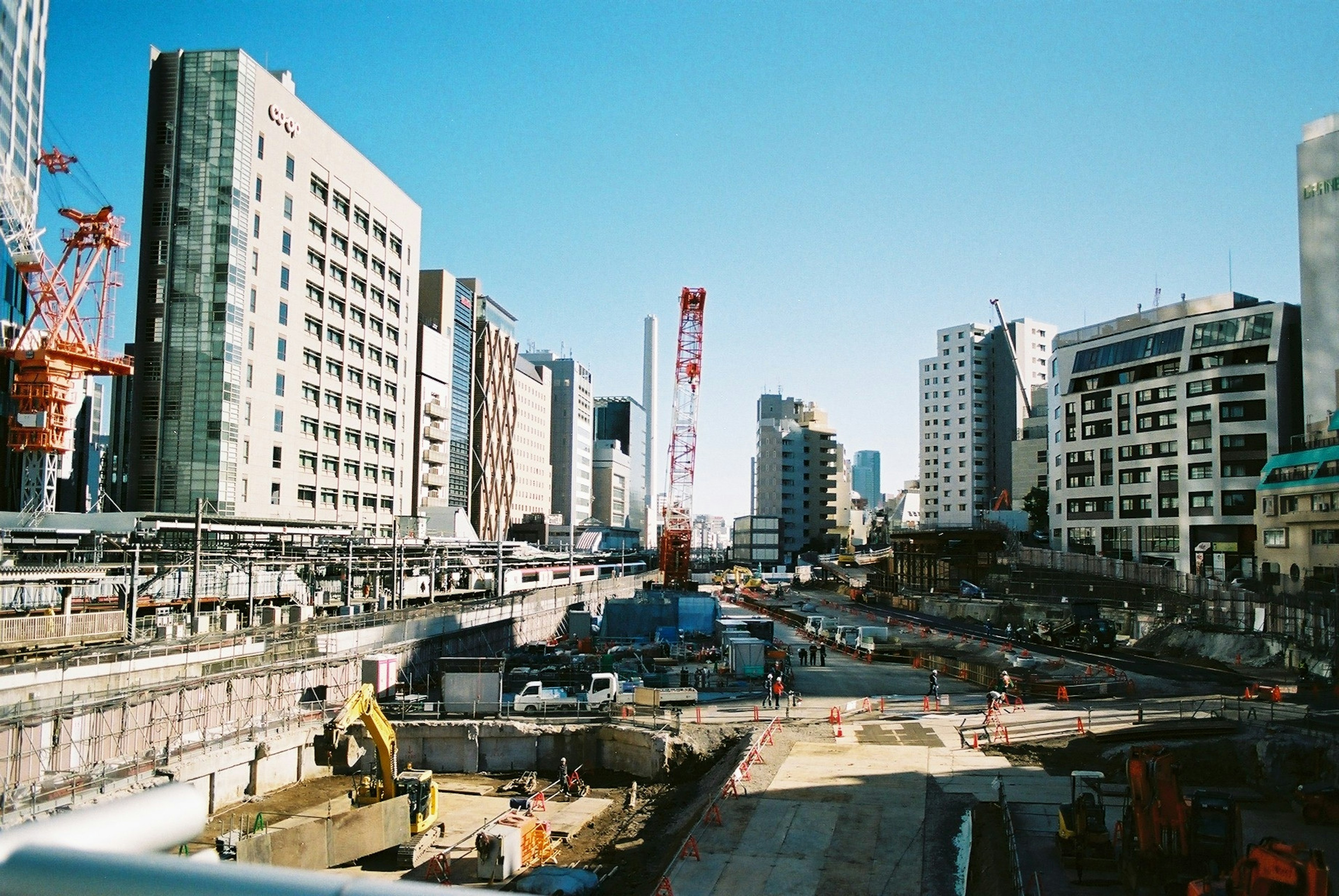 都市の建設現場と高層ビルの風景、青空の下でのクレーンと工事用車両