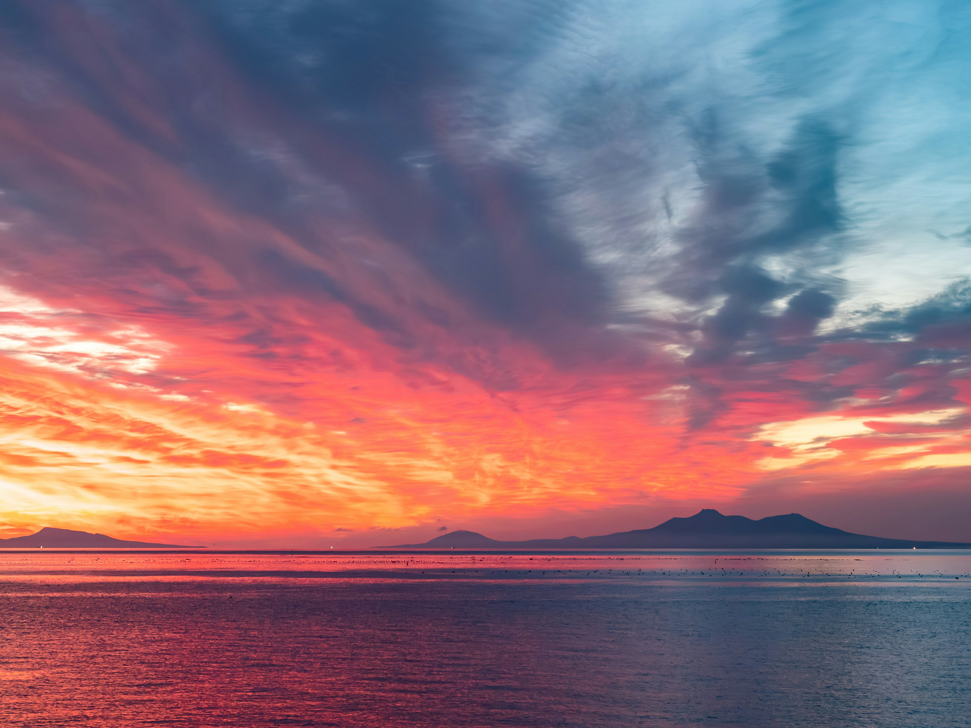 Stunning sunset with vibrant colors over calm sea and distant mountains