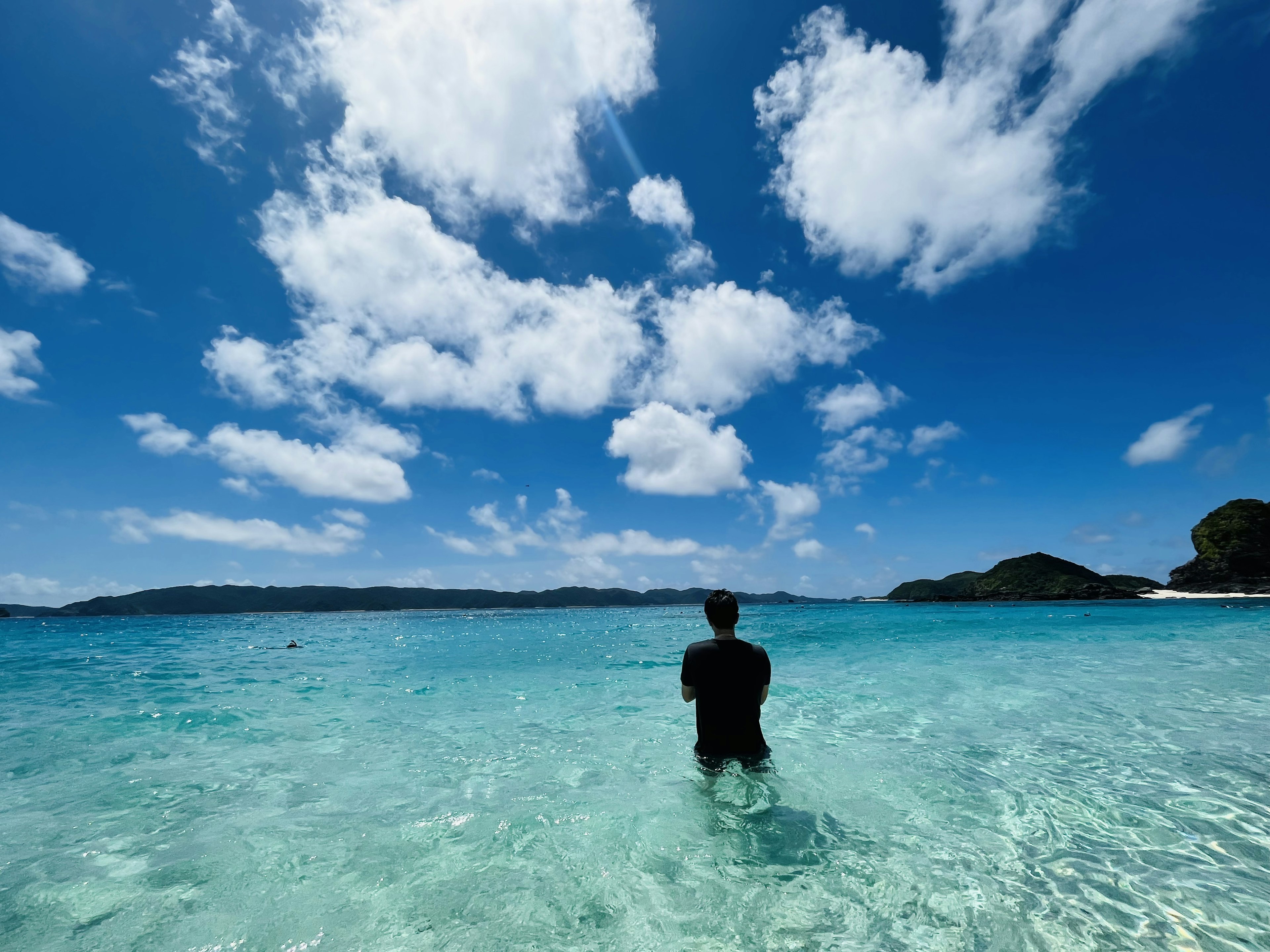 Person in black standing in clear blue water under a bright sky