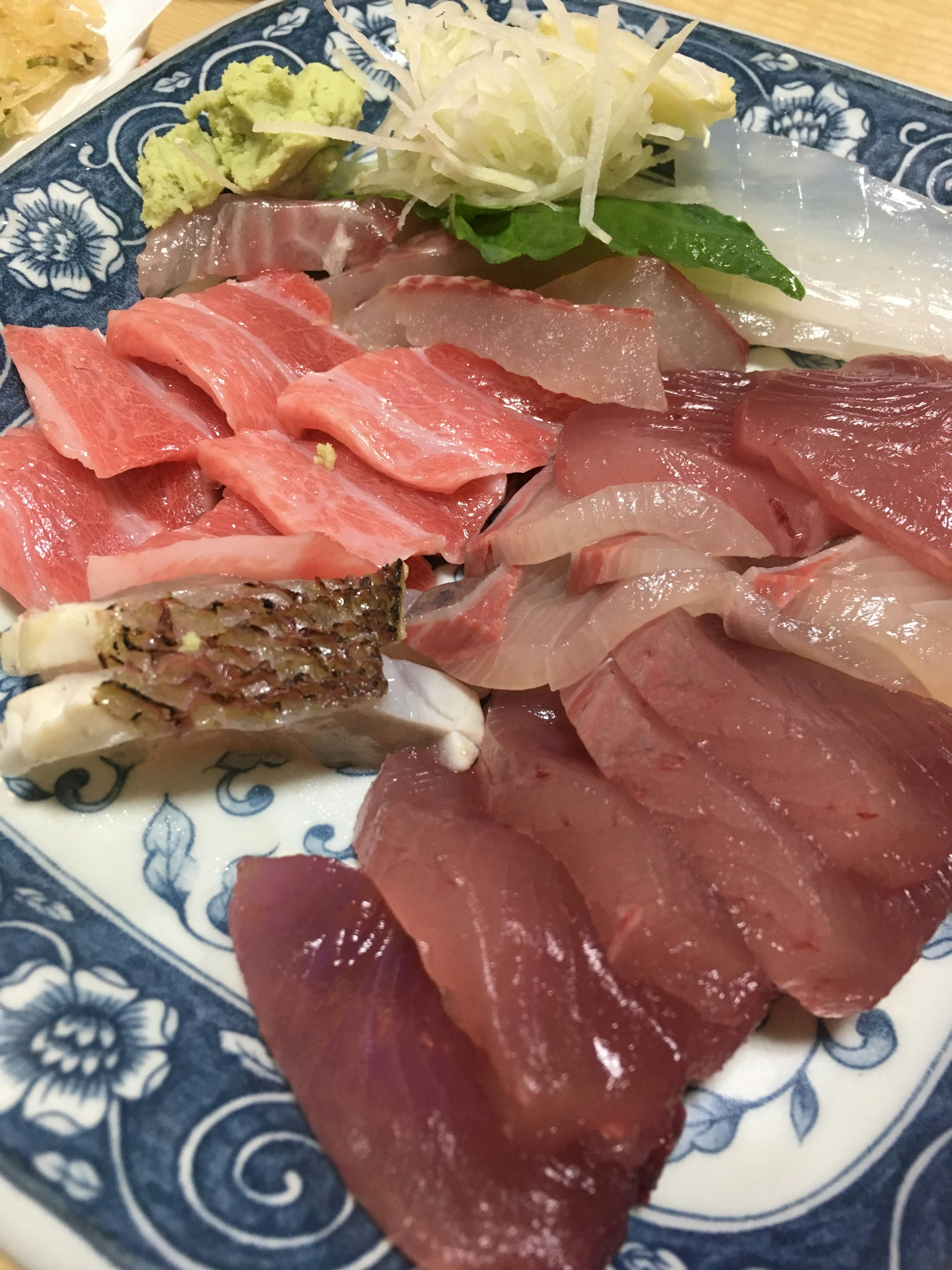 Fresh sashimi platter featuring various red and white fish on a blue plate with wasabi and ginger