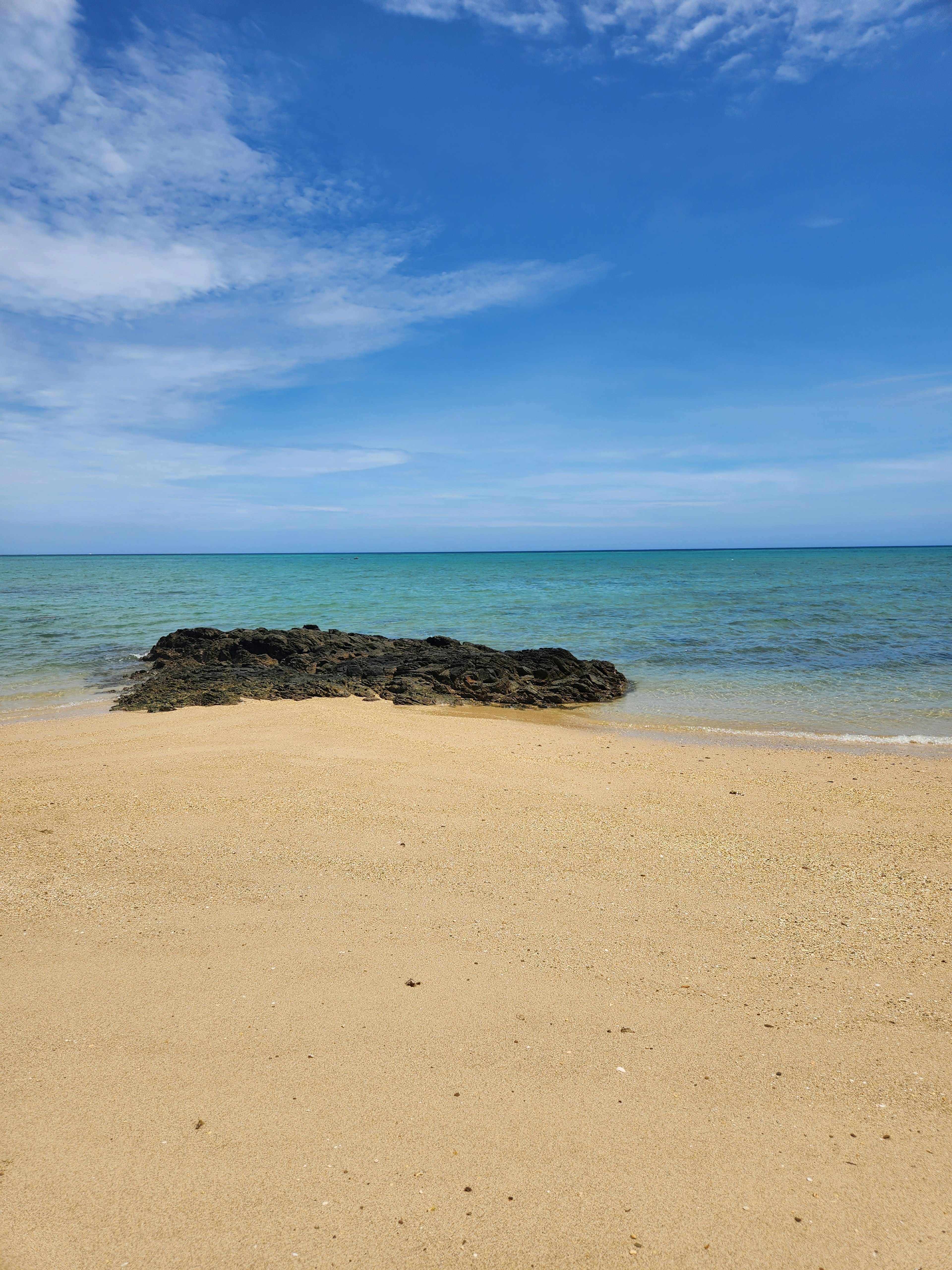 Eine Strandszene mit blauem Himmel und ruhigem Meer mit Sand und Felsen