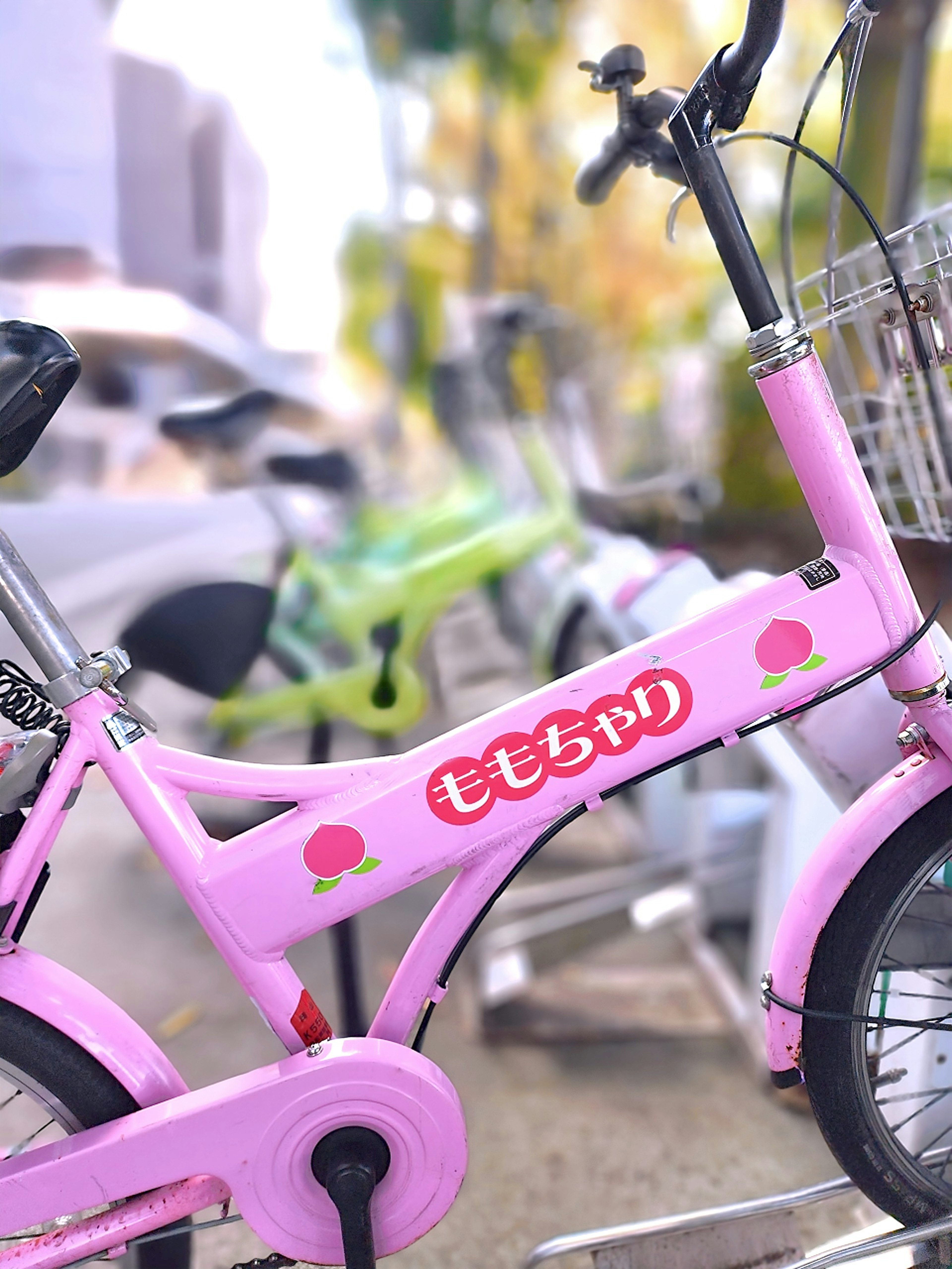 A pink bicycle with the name 'ももちゃん' written on it with other bicycles blurred in the background